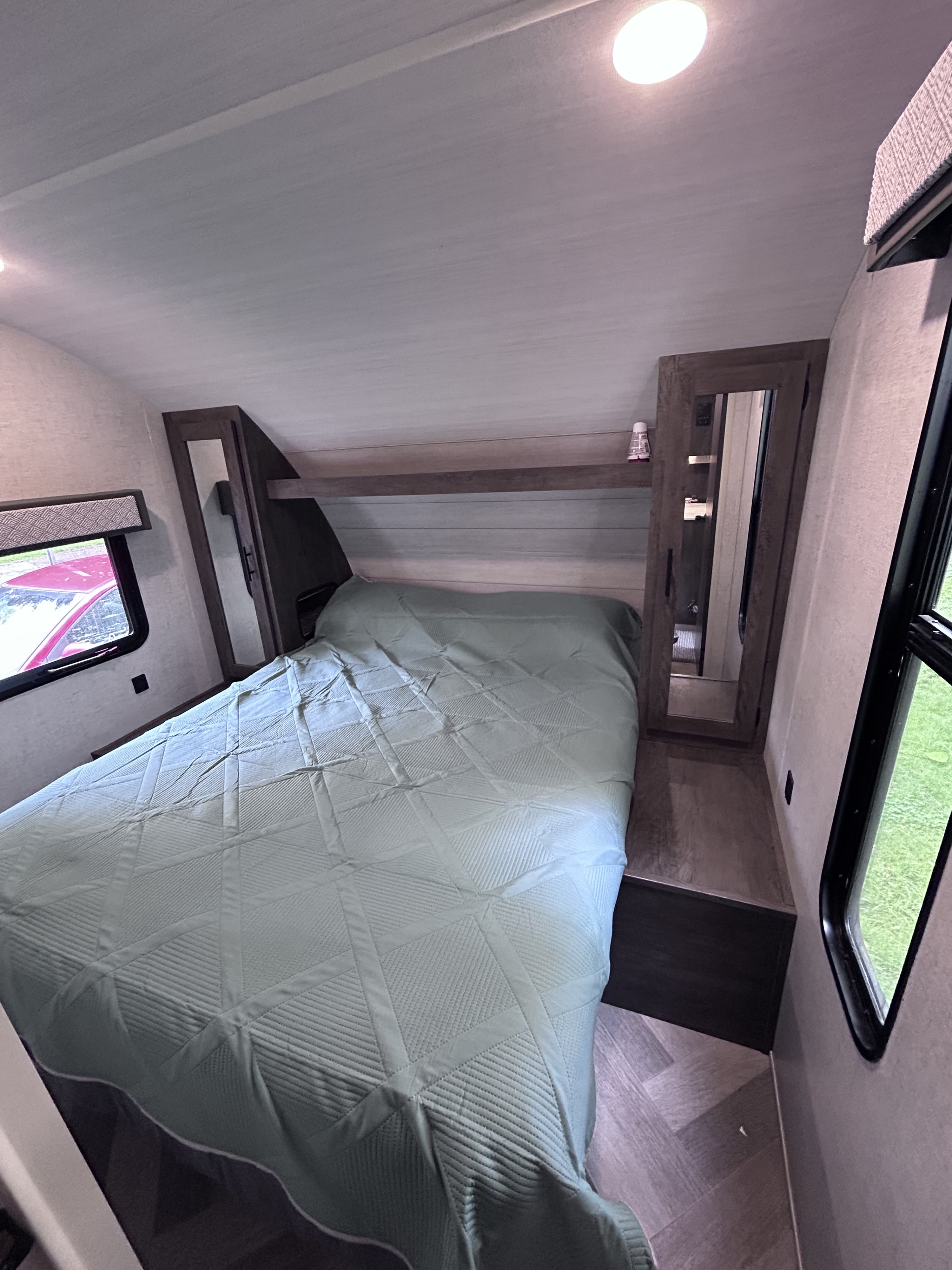 RV rental bedroom: a cozy interior with a patterned green bed, windows, and mirrored cabinet, optimized for travel comfort.. Forest River Wildwood X-Lite 2020