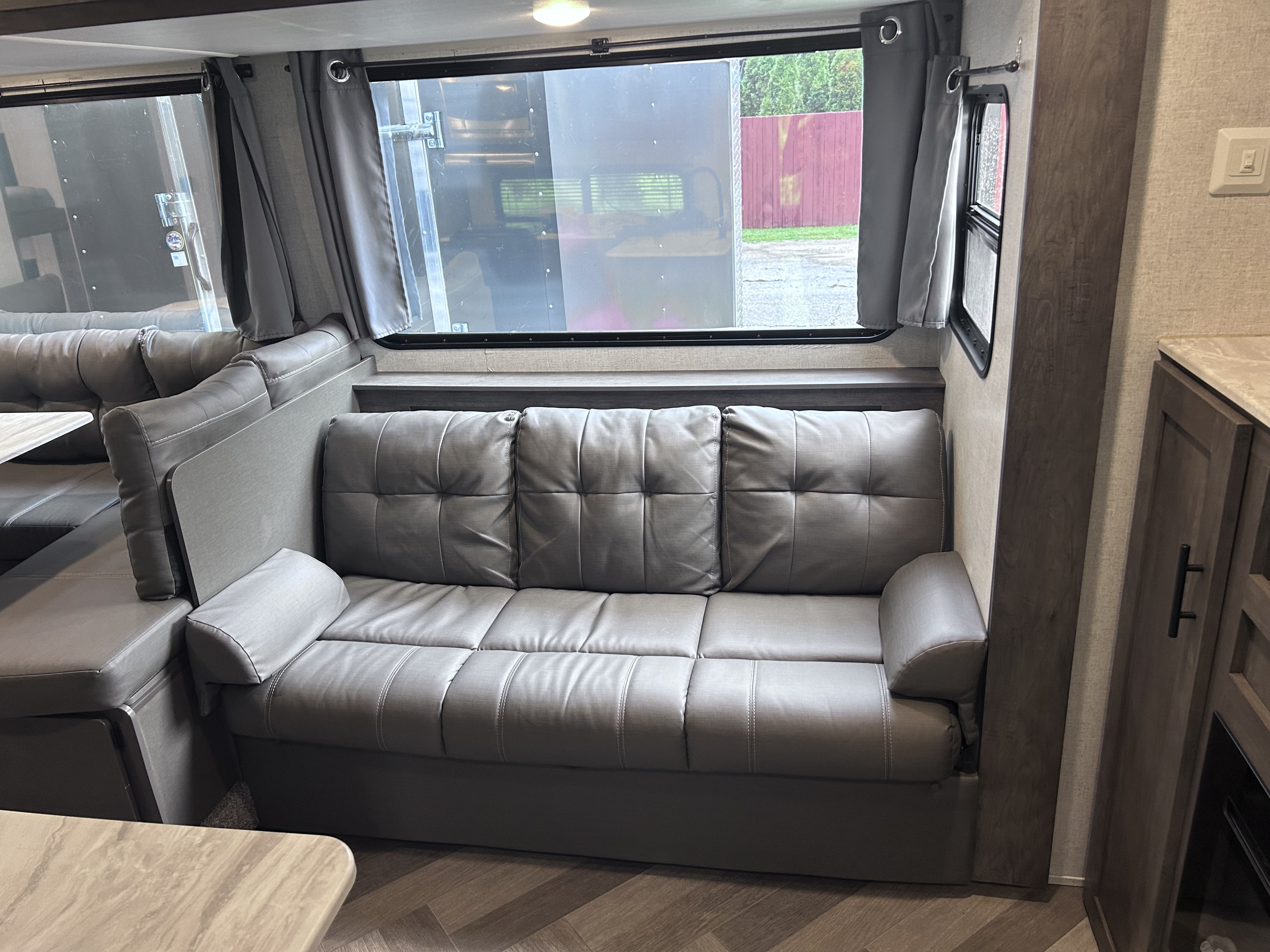 Spacious RV rental interior featuring a large gray sofa/dinette with windows and curtains, perfect for comfortable travel.. Forest River Wildwood X-Lite 2020