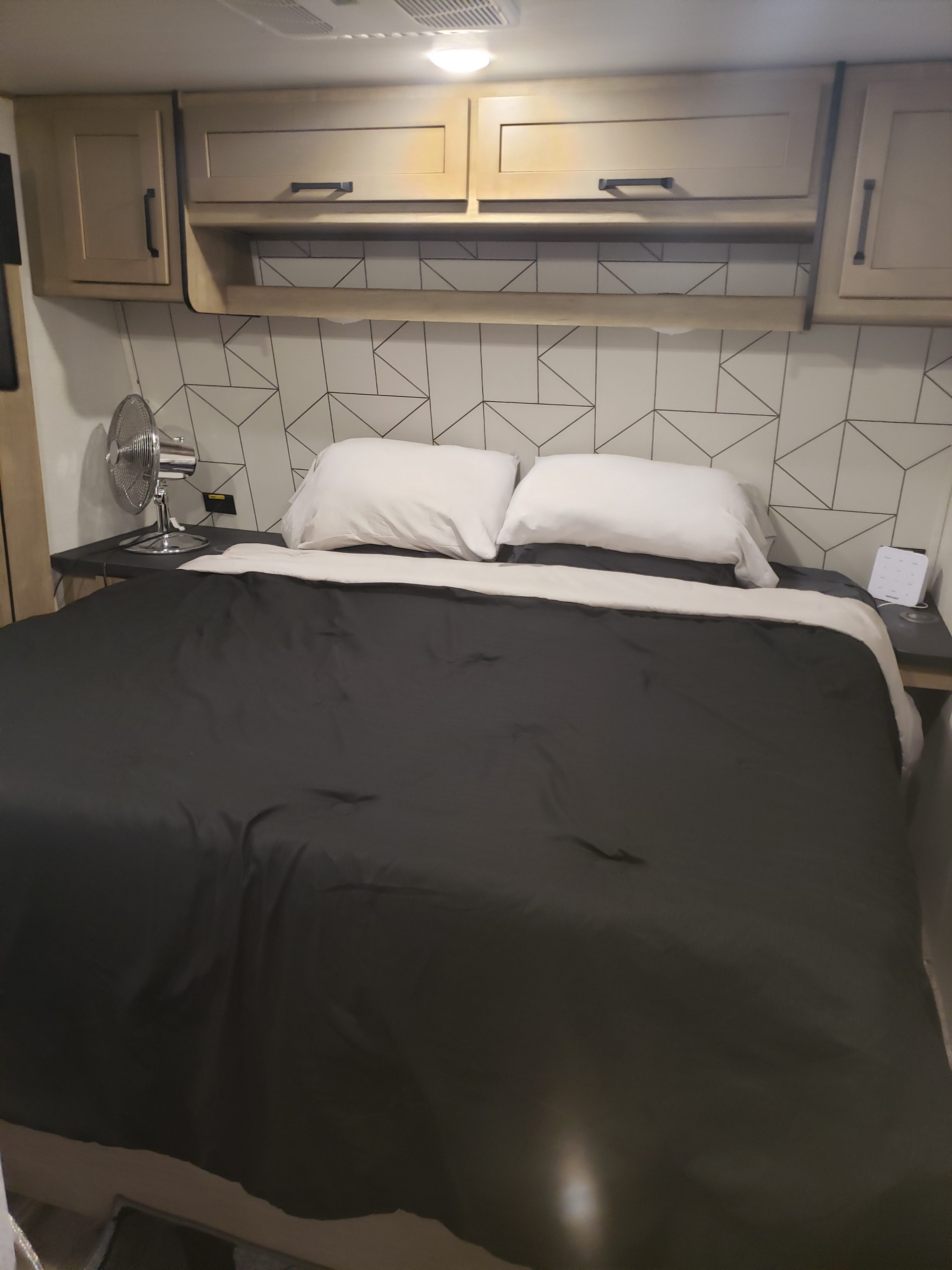 Modern rv rental bedroom with a comfy bed, sleek overhead cabinets, and geometric accent wall.. Keystone RV Raptor Toy Hauler 2022