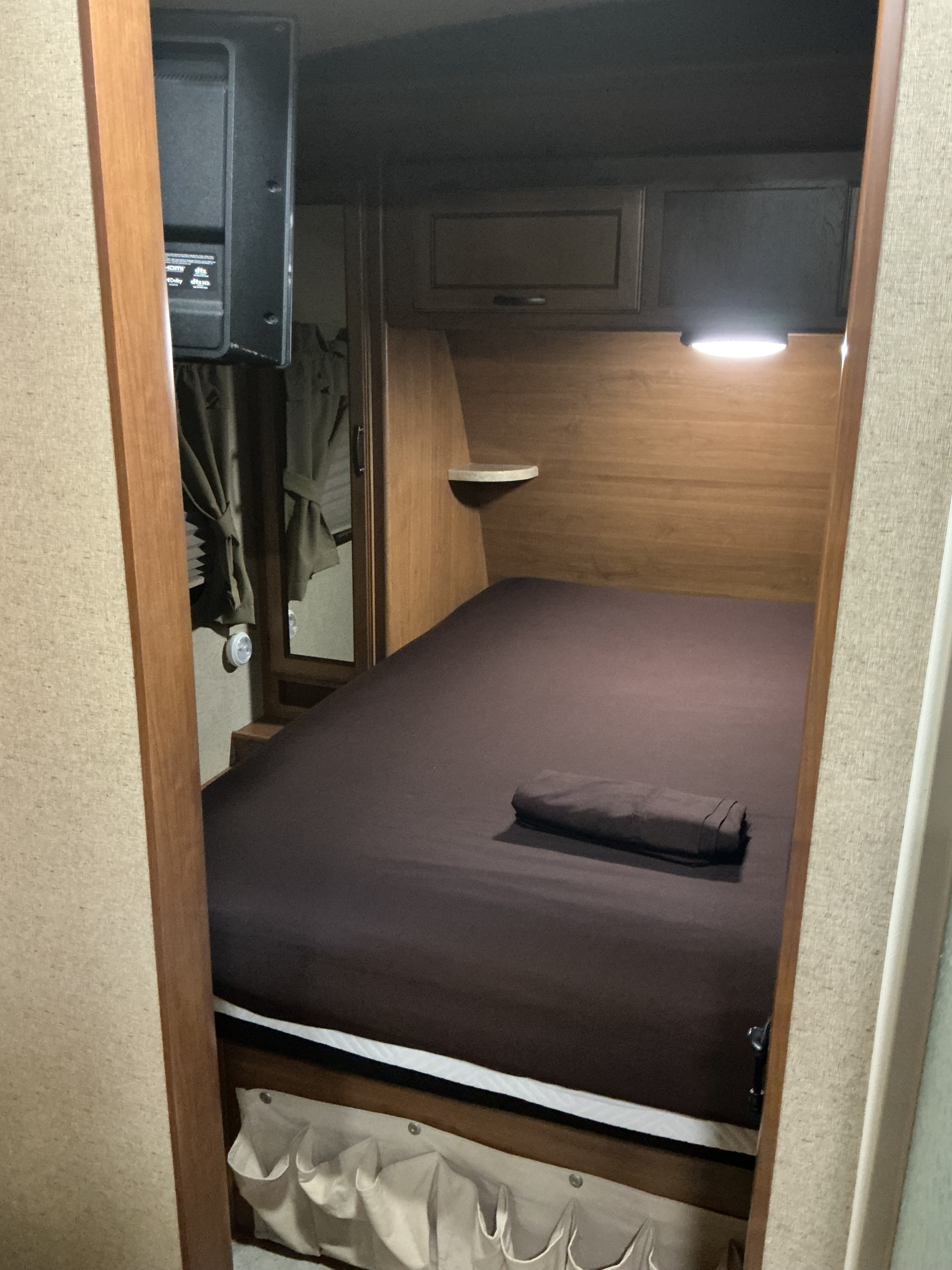 Cozy RV rental bedroom featuring a full-size bed, TV, overhead cabinets, and storage pockets. Perfect for compact travel.. Crossroads RV Sunset Trail Super Lite 2017