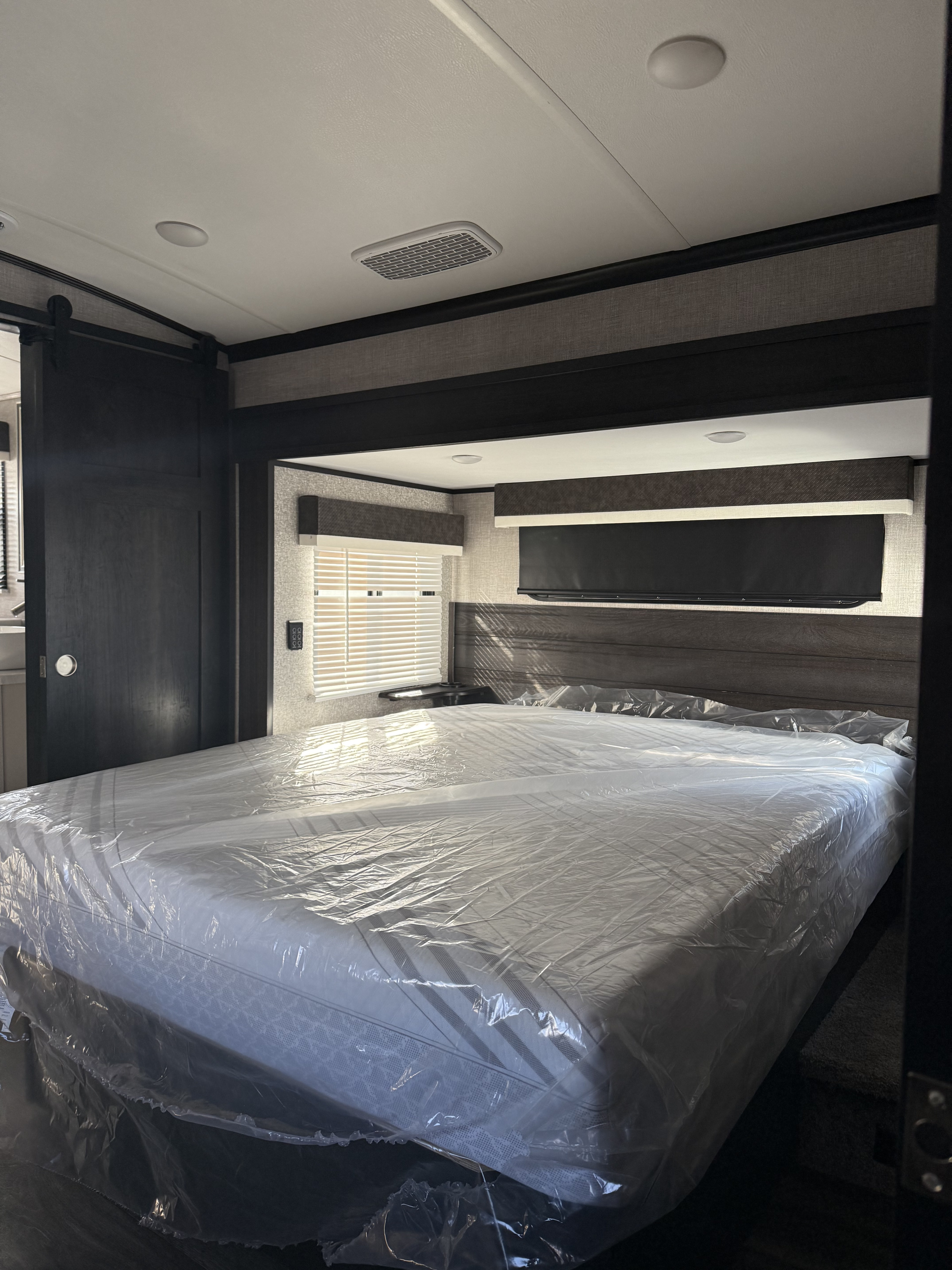 A clean, modern RV bedroom featuring a plastic-covered mattress on a large bed, ideal for your next rv rental.. Jayco North Point 2021