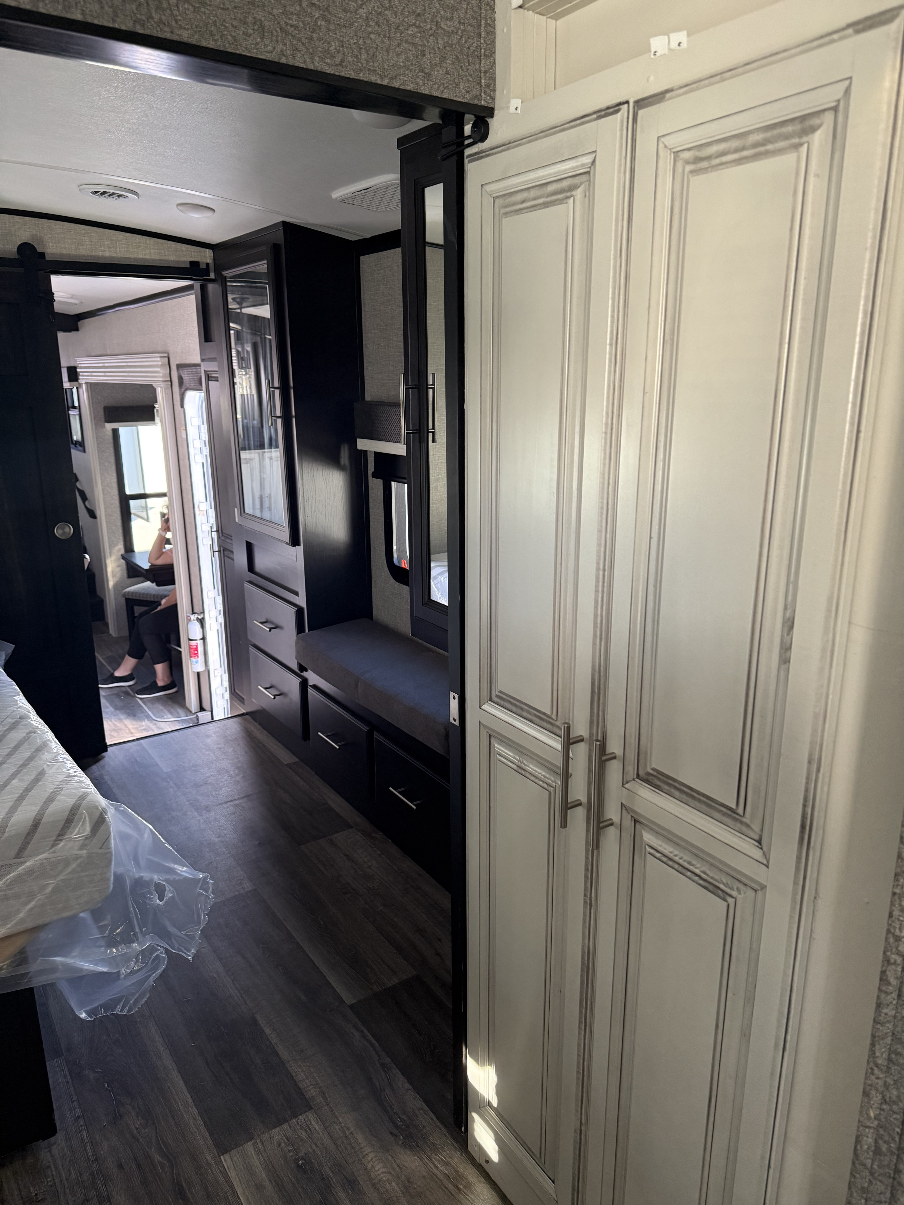 Modern RV rental interior with distressed white cabinets, dark wood-look flooring, and built-in furniture leading to the dining area.. Jayco North Point 2021