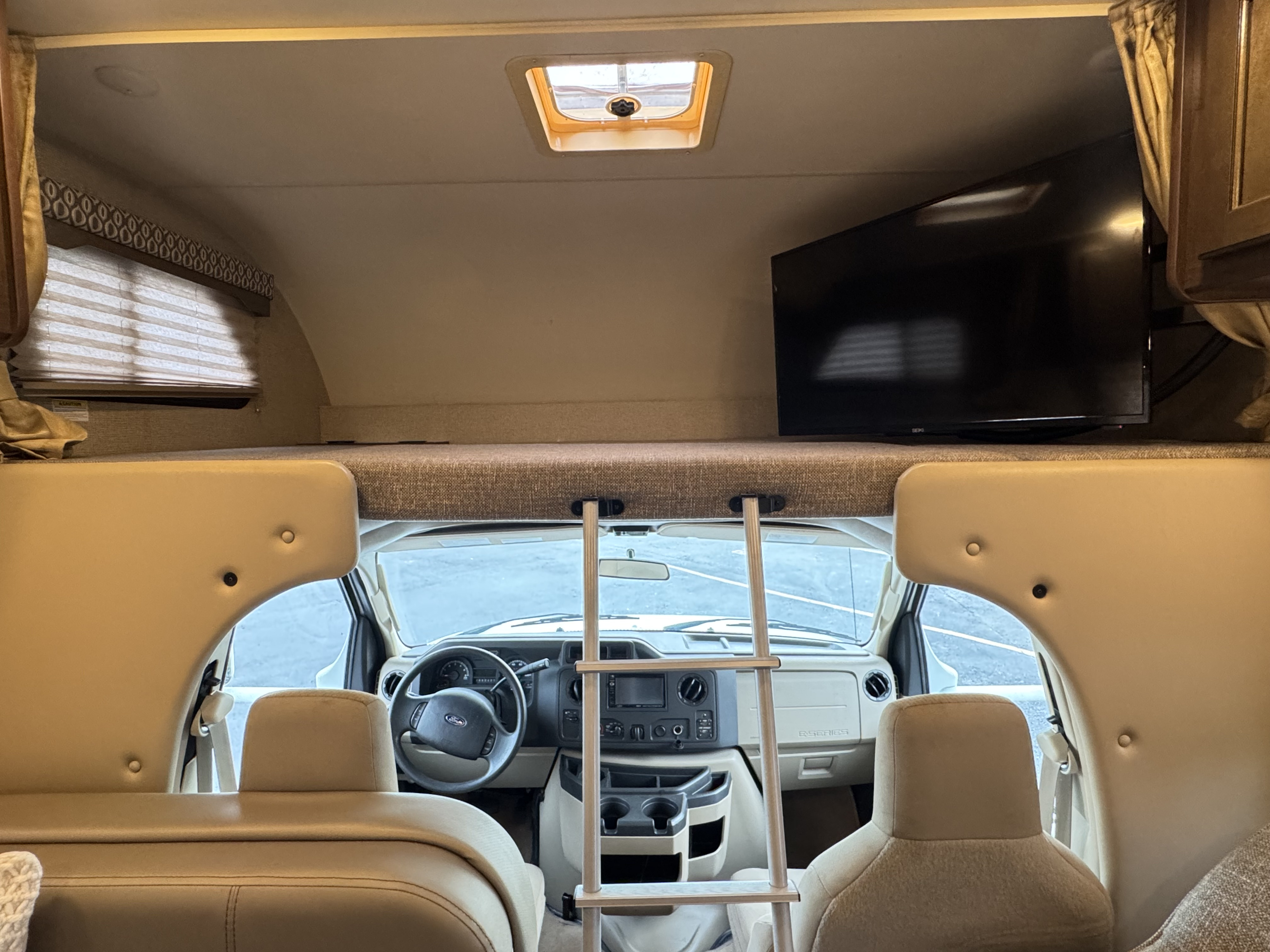 RV rental interior: an overhead sleeping bunk with TV and ladder is above the driver's cab area.. Thor Freedom Elite 2017