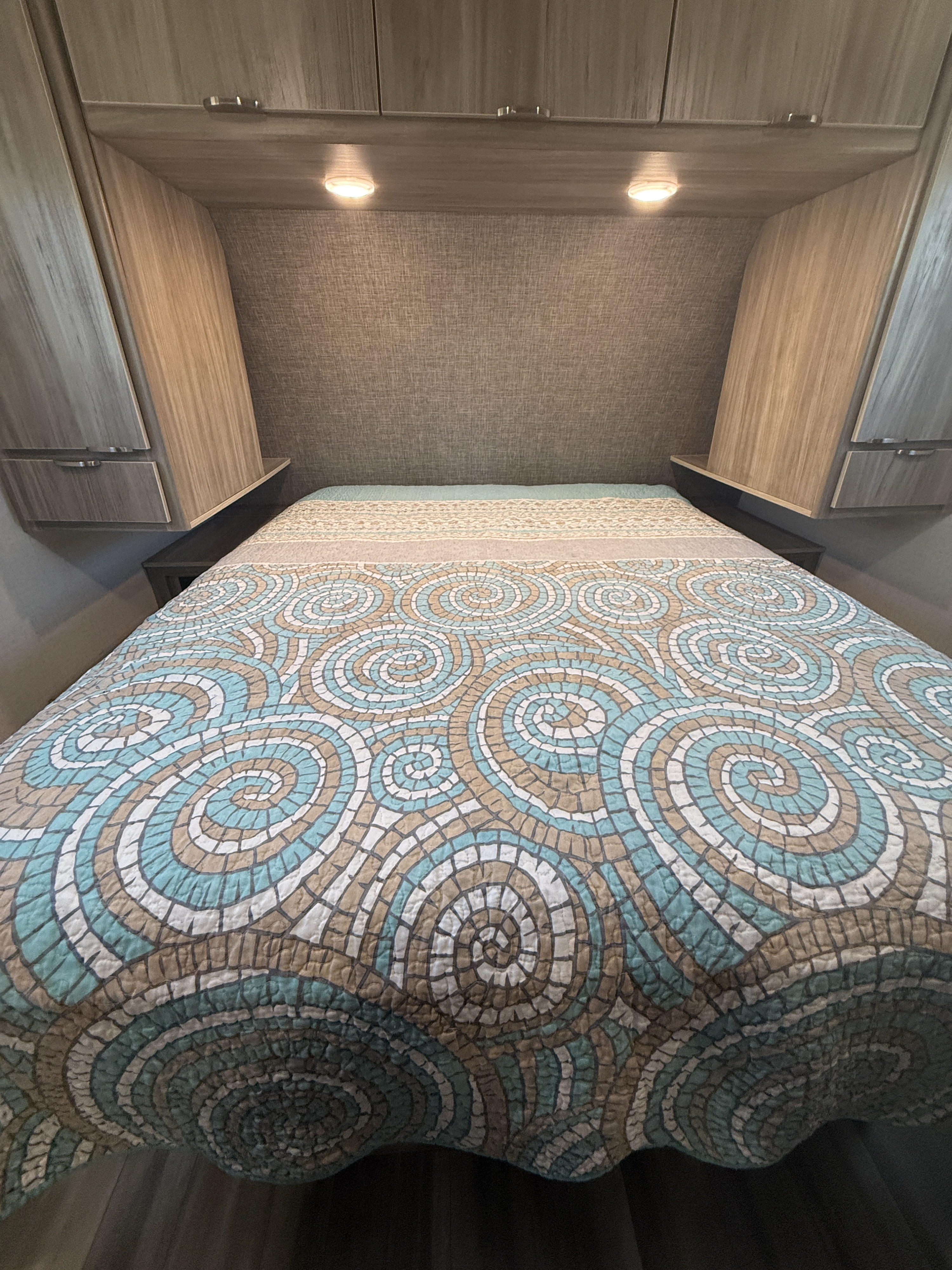 Comfortable RV rental bedroom showcasing a mosaic-patterned quilt, sleek overhead cabinets, and practical bedside lights.. Winnebago Mini Winnie 2022