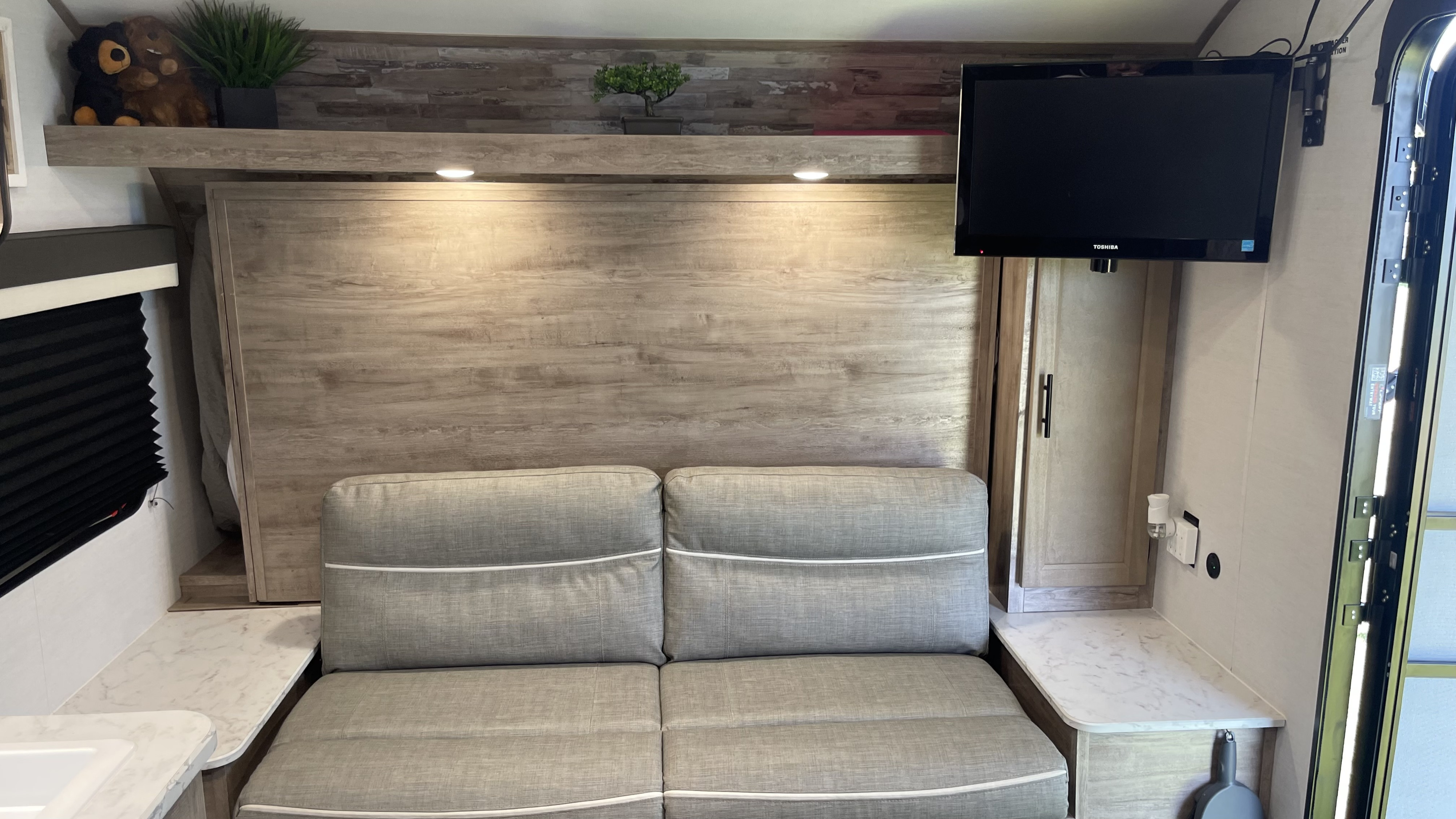 Inside an RV rental, showing a comfortable sofa, wall-mounted TV, and a hidden Murphy bed system.. Gulf Stream Grand River 22Mb 2024