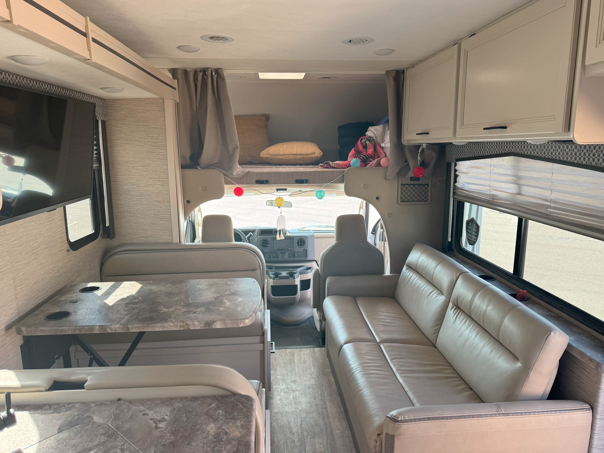 Spacious RV rental interior featuring a dinette, comfortable sofa, and cozy overhead bunk.. Thor Chateau 2023