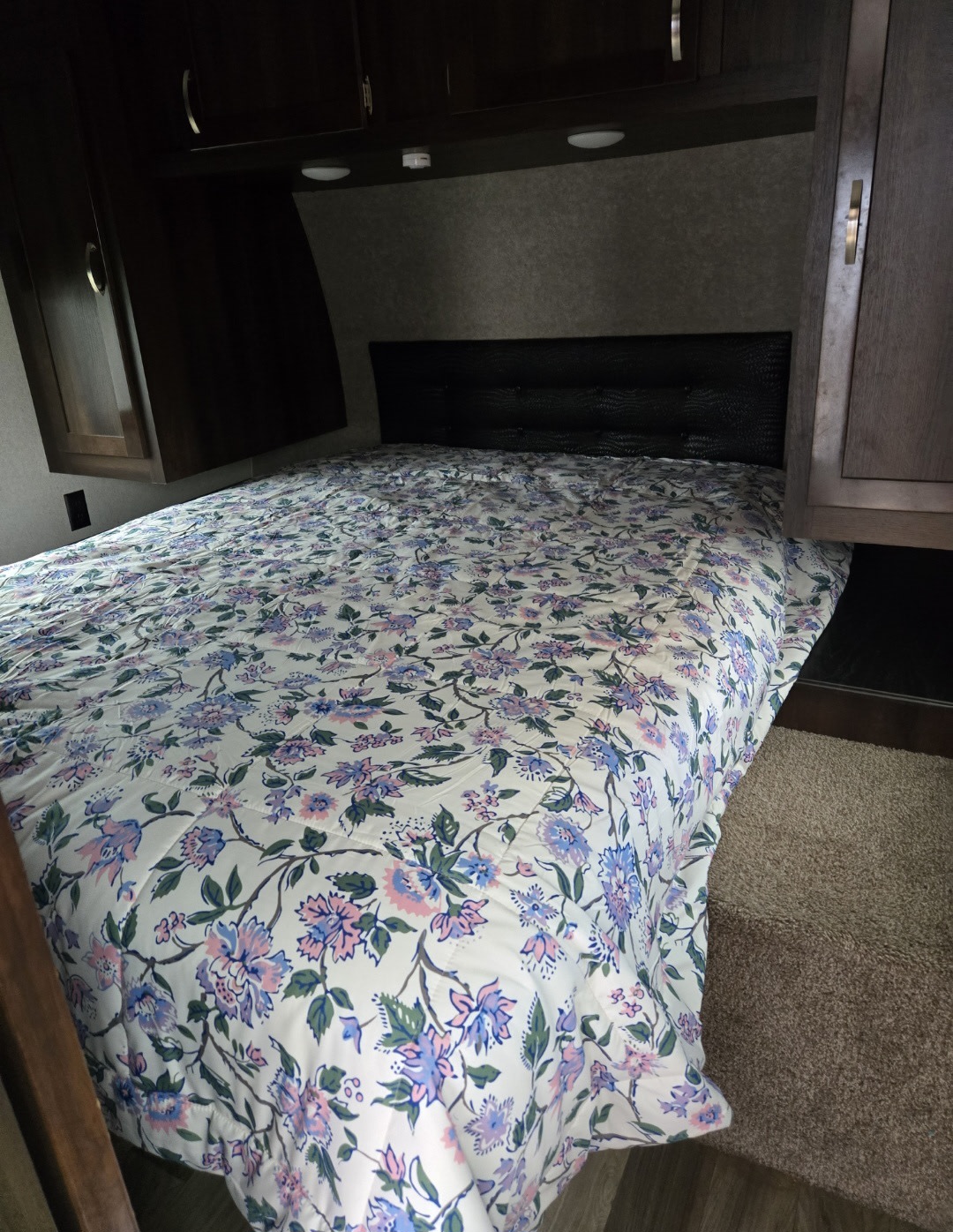 Bedroom in an RV rental, featuring a bed with floral comforter, cabinets, and soft lighting for cozy travel.. Jayco Octane 2018