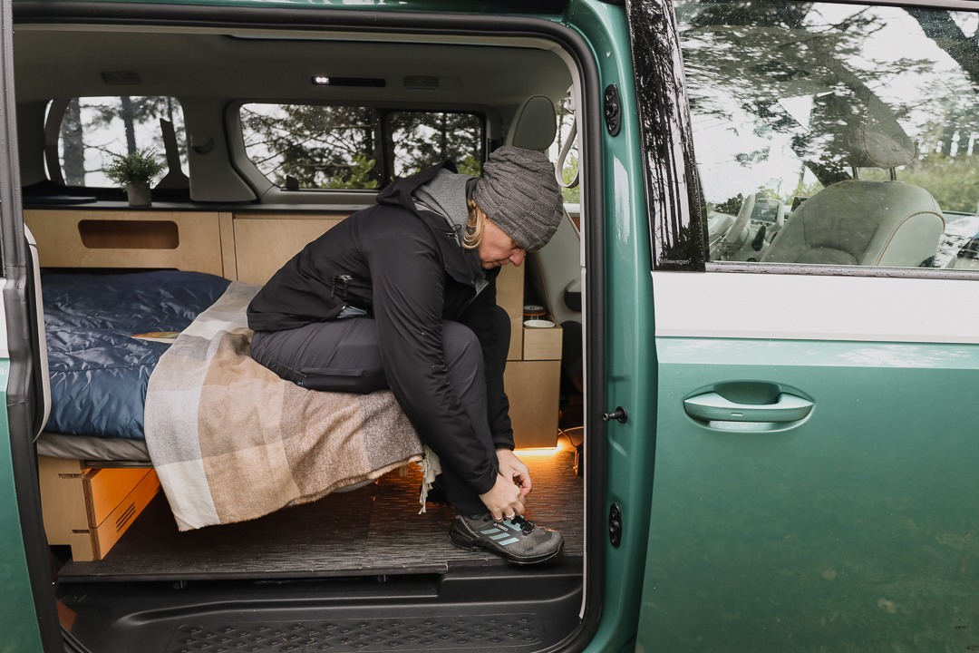 Inside a green RV rental, a person on the bed ties a shoe. Cozy camper interior for outdoor adventure.. Volkswagen Other 2025