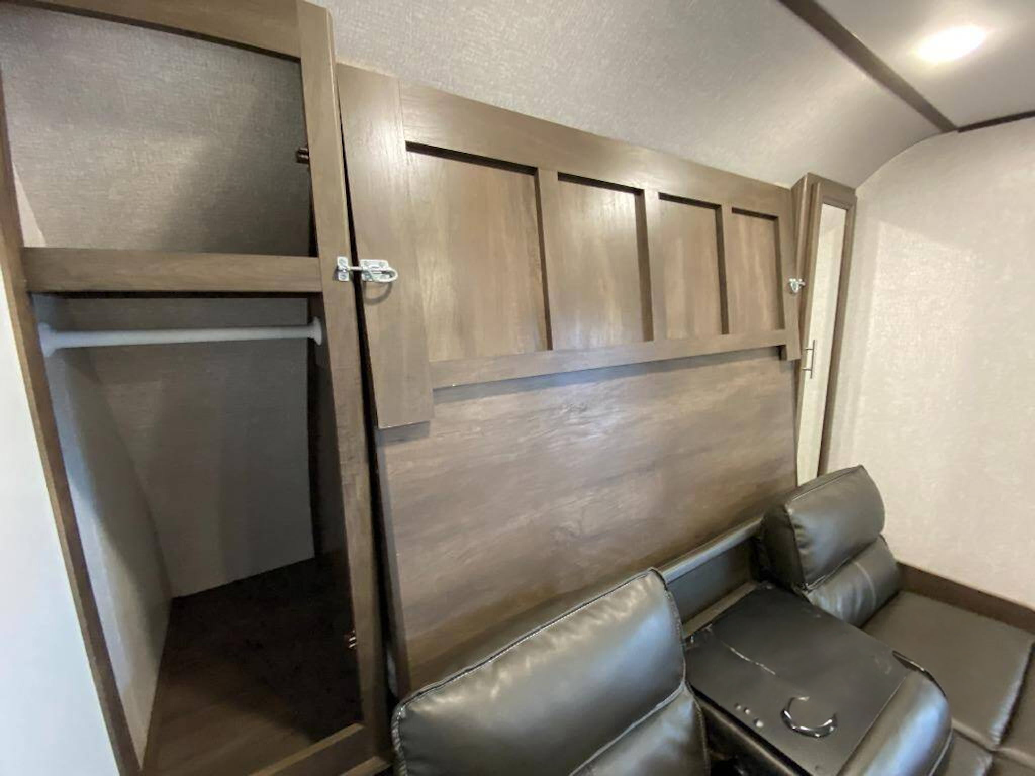 RV rental interior: Wooden closet with hanging rod, and black leather reclining seating with a console.. Coleman 2125bh 2019