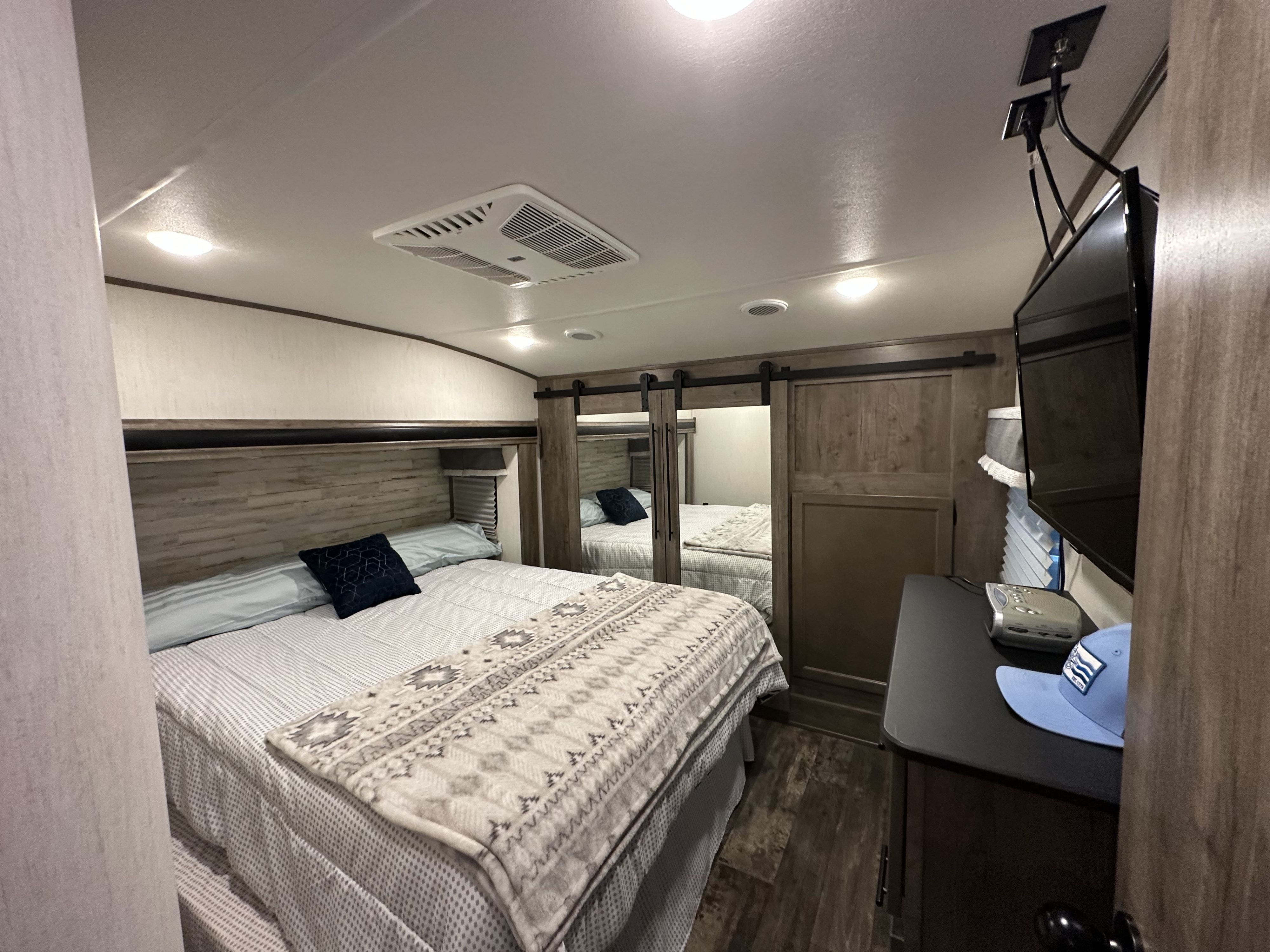 RV rental bedroom featuring a comfy bed, overhead AC, TV, and mirrored closet doors.. Forest River Sabre 2021
