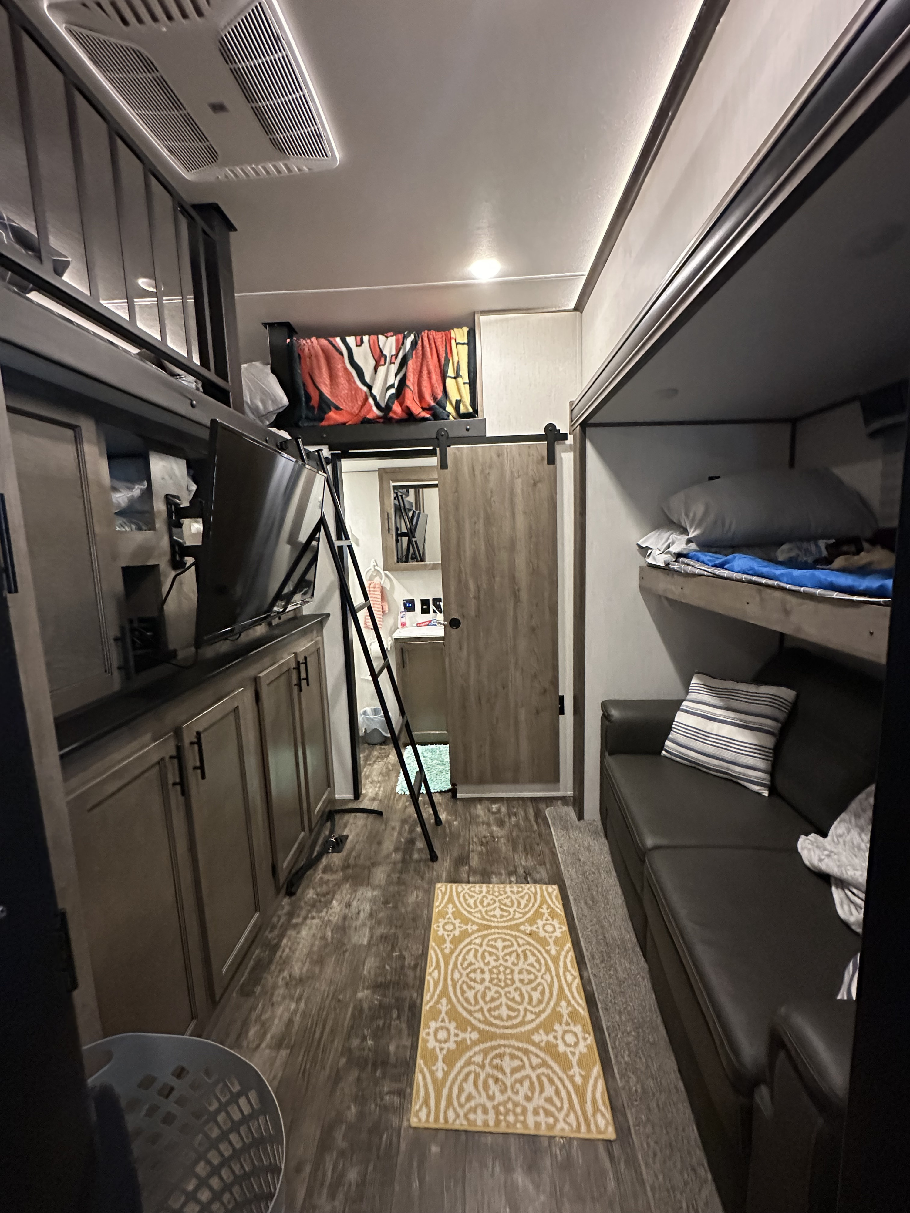 RV rental: Interior showing a loft bed, bunk beds, sofa, TV, wood floor, and a bathroom accessible via a barn door.. Forest River Sabre 2021