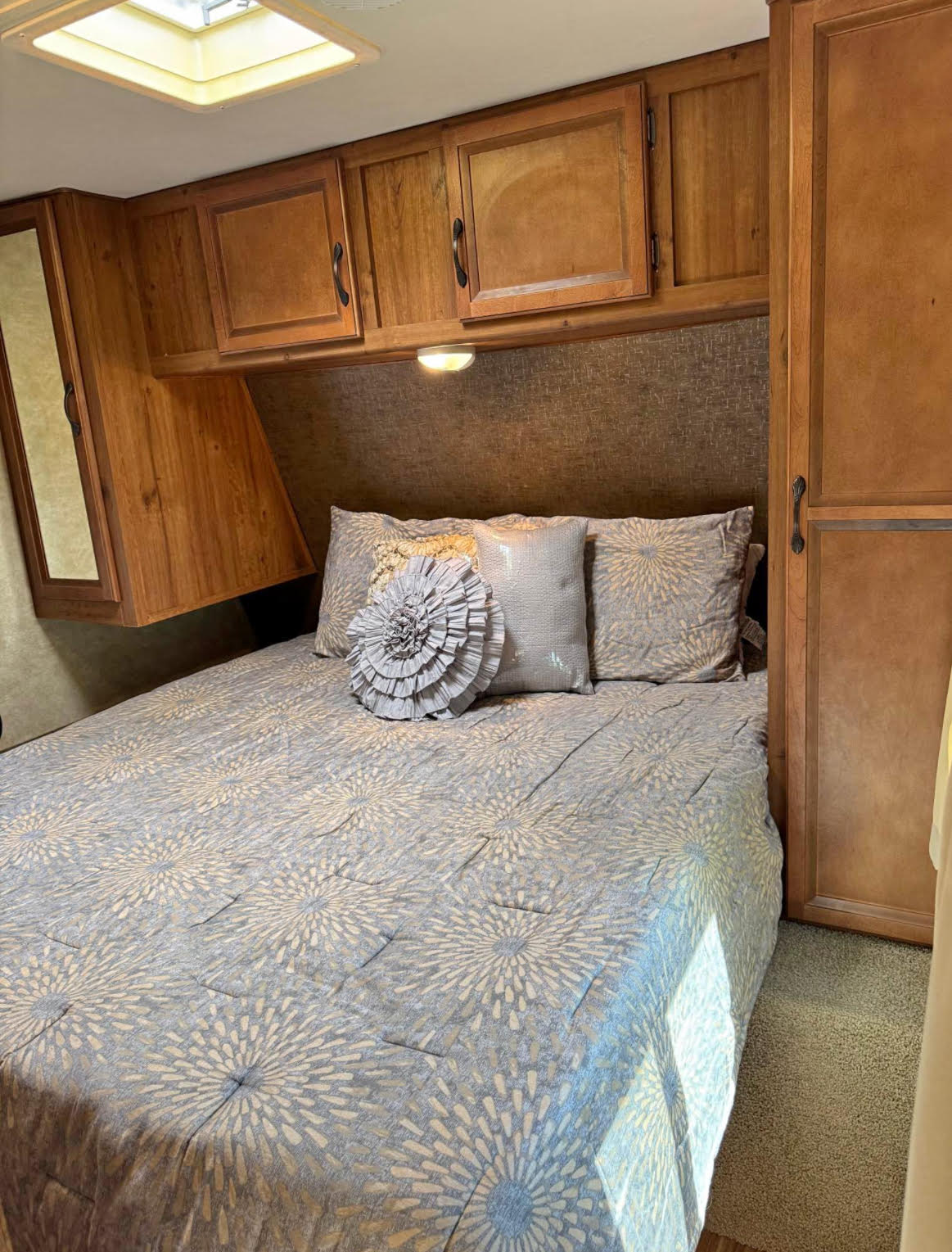 Comfortable RV rental bedroom showcasing a patterned bed, overhead wood cabinets, ample storage, and a skylight.. Gulf Stream Innsbruck 2015