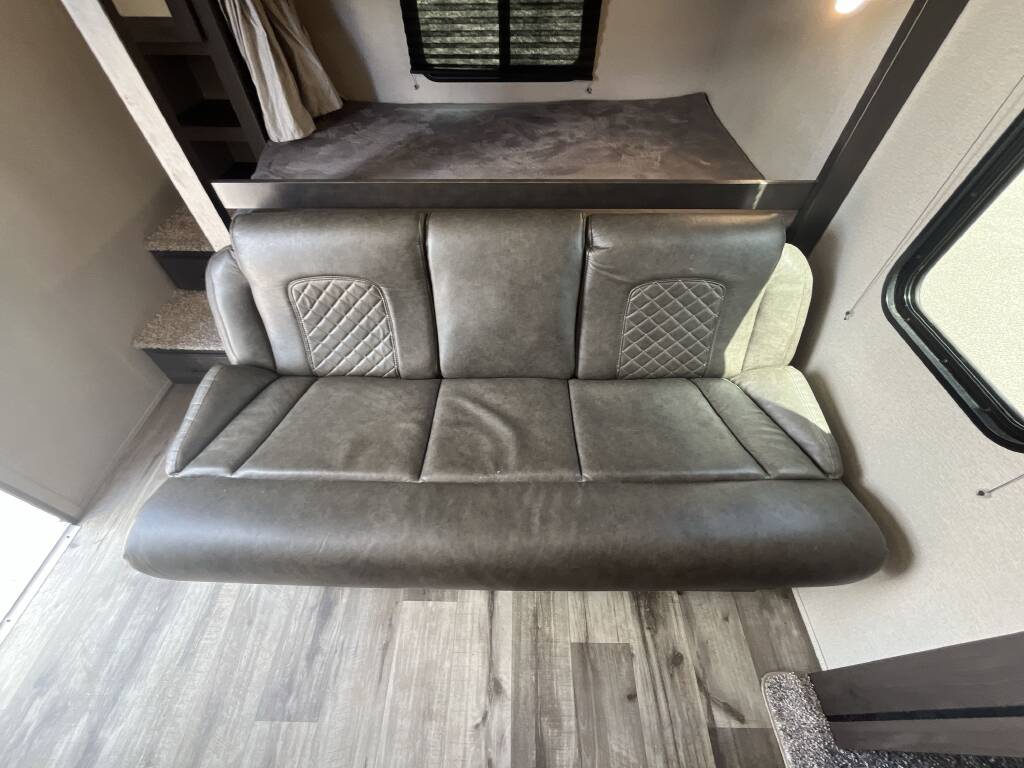 Cozy RV rental interior: A gray three-seater sofa with quilted accents is beneath a bunk bed, offering functional living and sleeping space.. Grand Design Transcend Xplor 2023