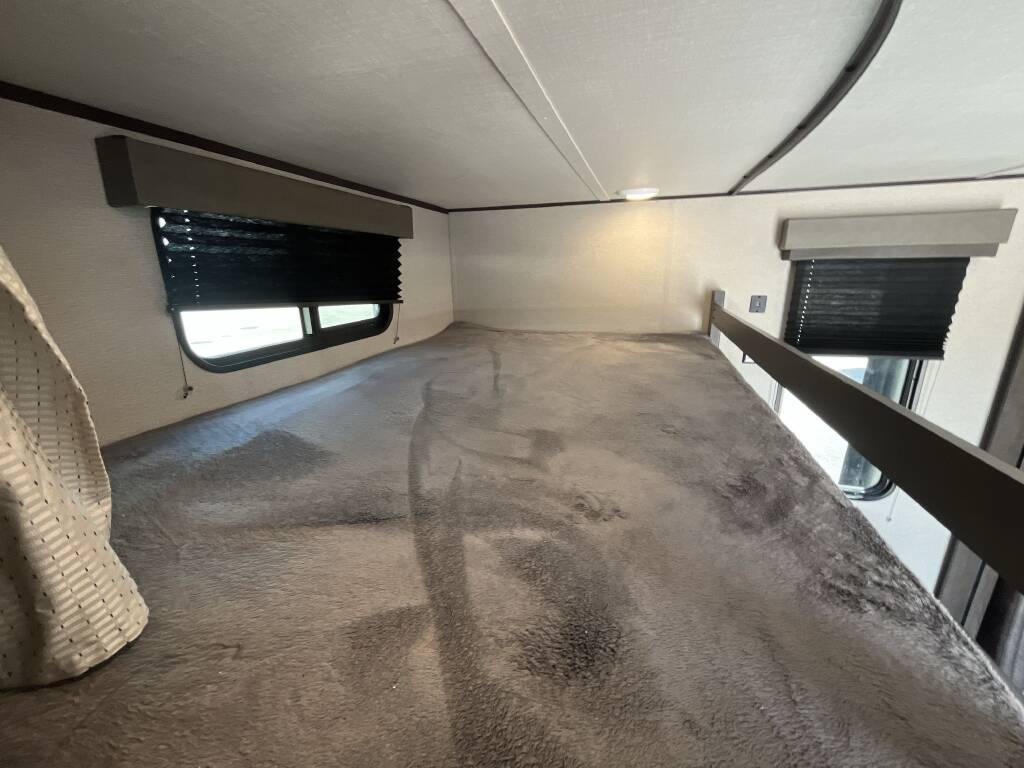 Comfortable top bunk bed in an RV rental, featuring cozy bedding and windows with privacy blinds.. Grand Design Transcend Xplor 2023