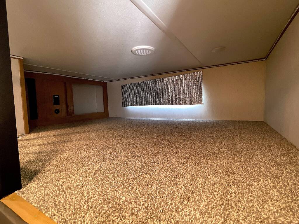 Inside an RV rental: a cozy, carpeted loft sleeping space with light walls, a wooden panel, and a mesh screen.. Forest River Sabre 2024