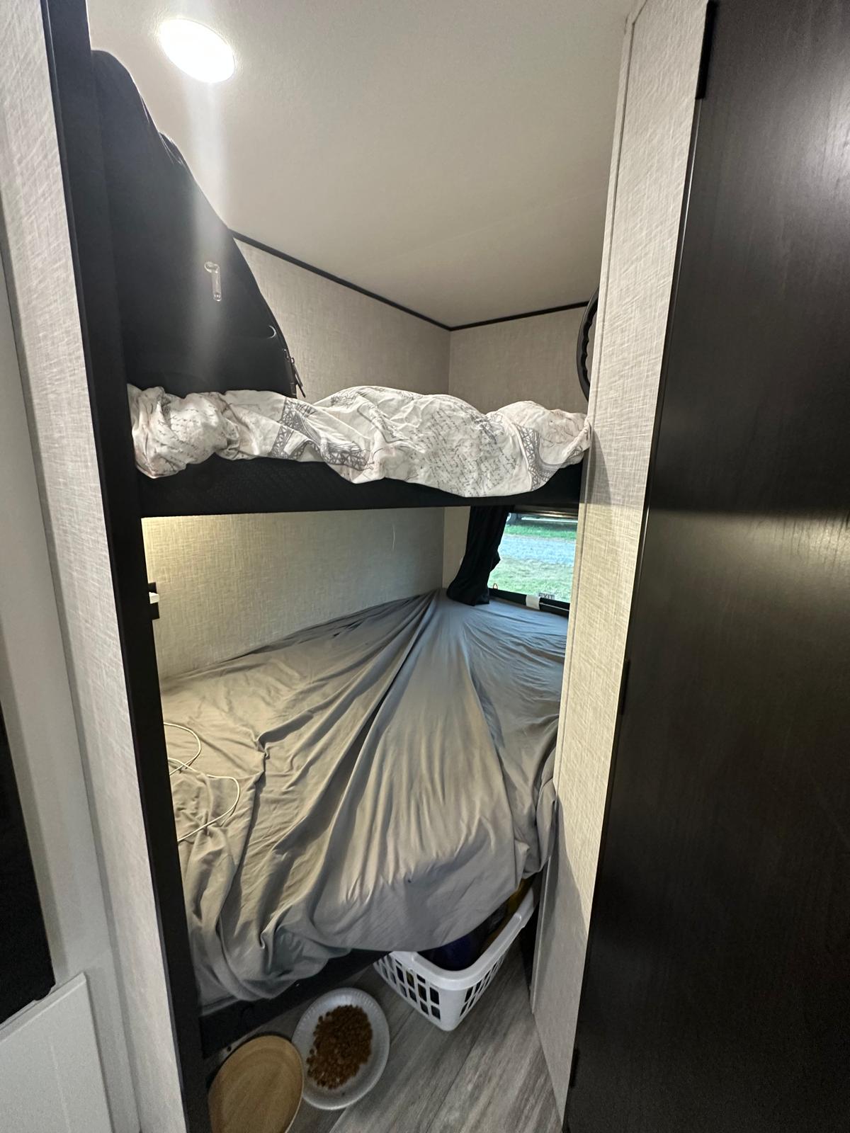 Compact RV rental interior featuring stacked bunk beds, a window with outdoor views, and pet bowls on the floor.. Jayco Jay Flight SLX 2025