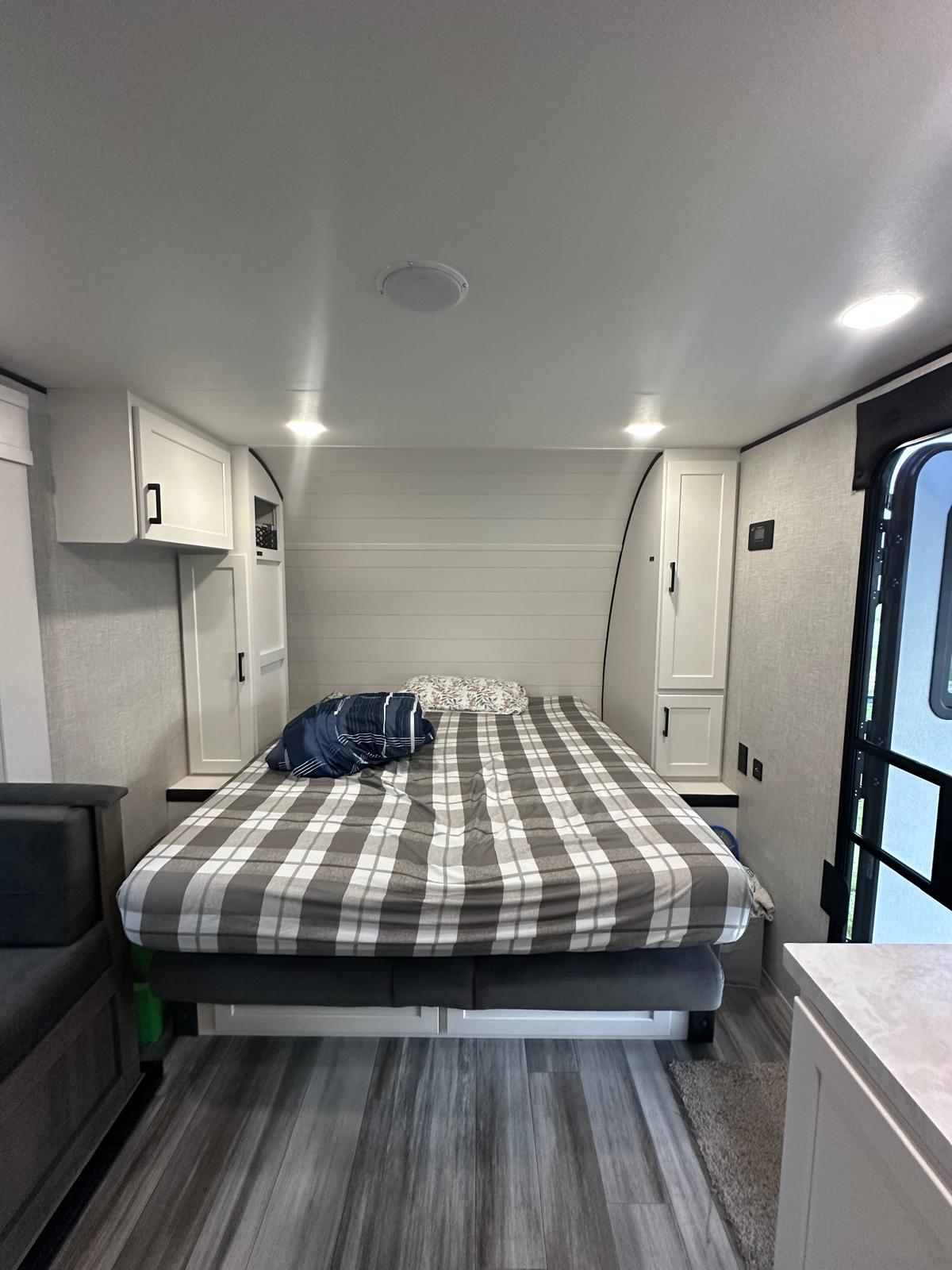 RV rental bedroom setup: a comfortable plaid bed flanked by white cabinets, with modern wood-look flooring. Ready for your adventure.. Jayco Jay Flight SLX 2025