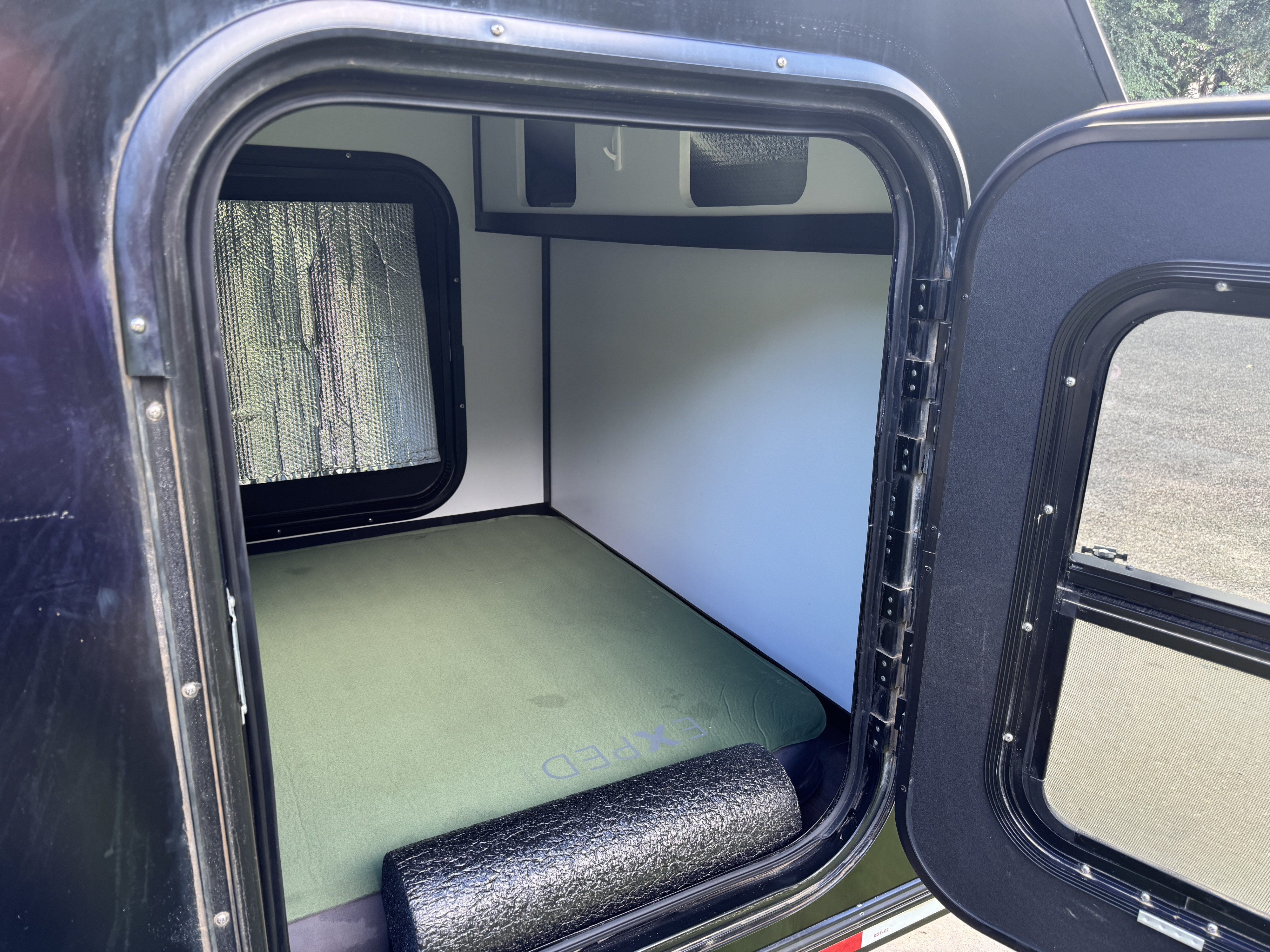 Cozy teardrop RV rental interior: green sleeping pad, window sunshade, and foam roller visible.. Tiny Camper Company 5x8 Kong Squaredrop Trailer 2023