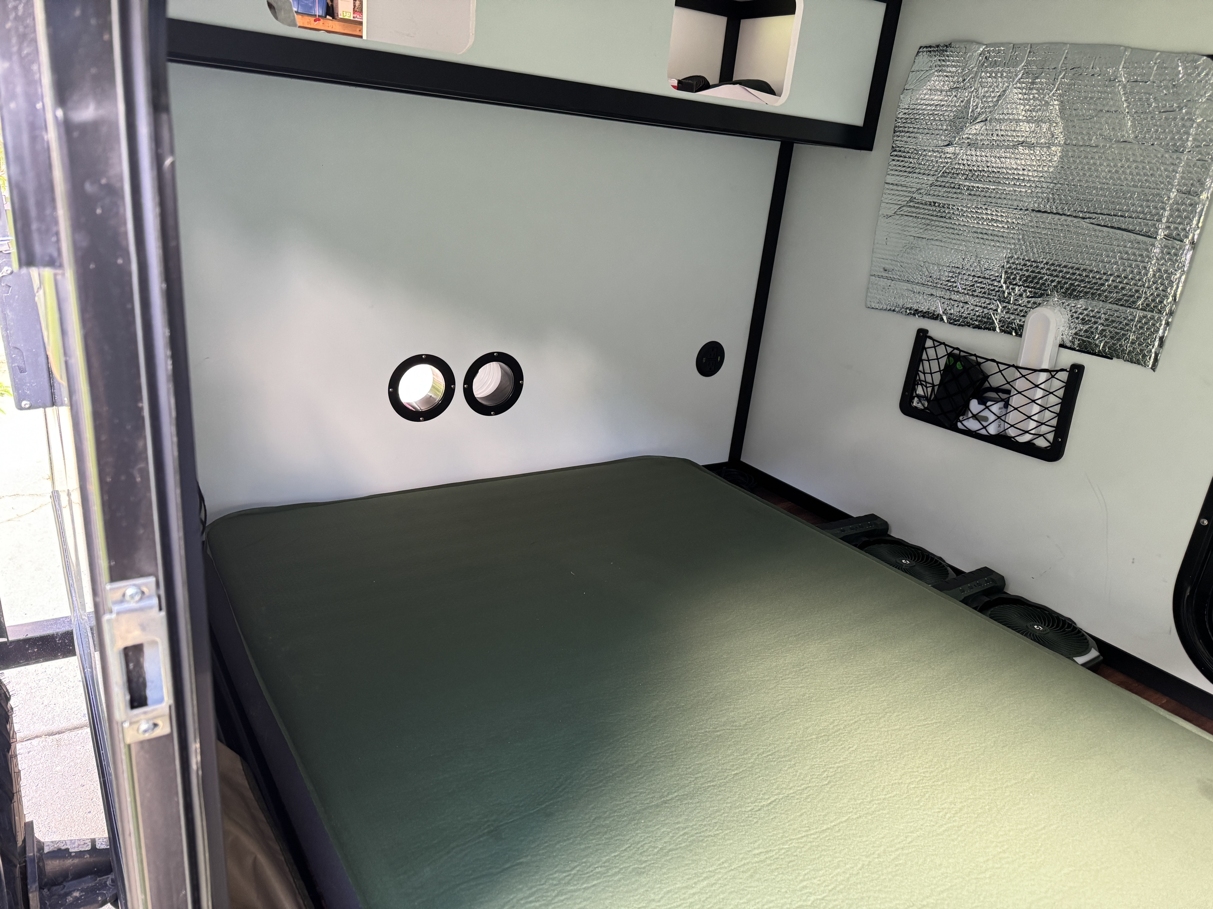 RV rental interior: A compact sleeping area with a green mattress, wall vents, cooling fans, and mesh storage.. Tiny Camper Company 5x8 Kong Squaredrop Trailer 2023