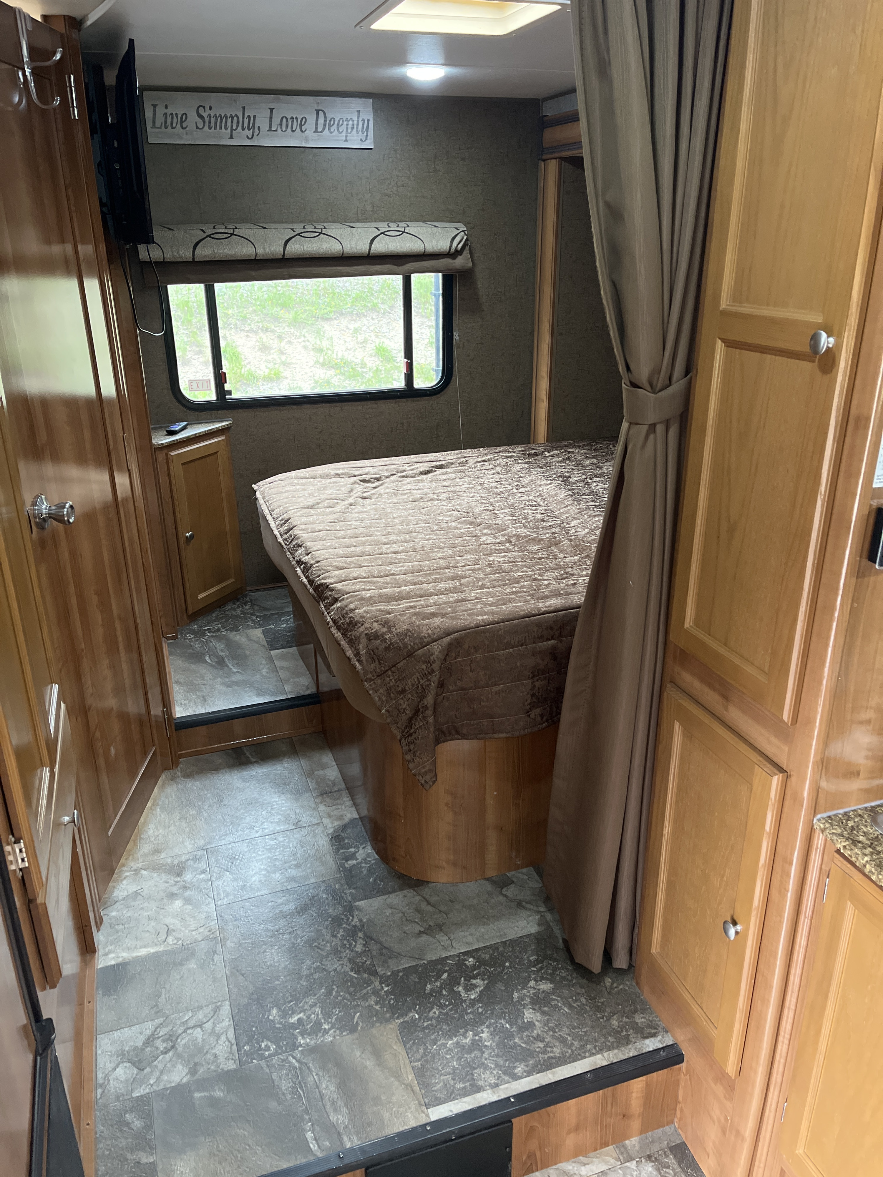 Cozy RV rental bedroom with a large bed, window, mounted TV, and a "Live Simply, Love Deeply" wall sign.. Forest River Coachmen Leprechaun 2018
