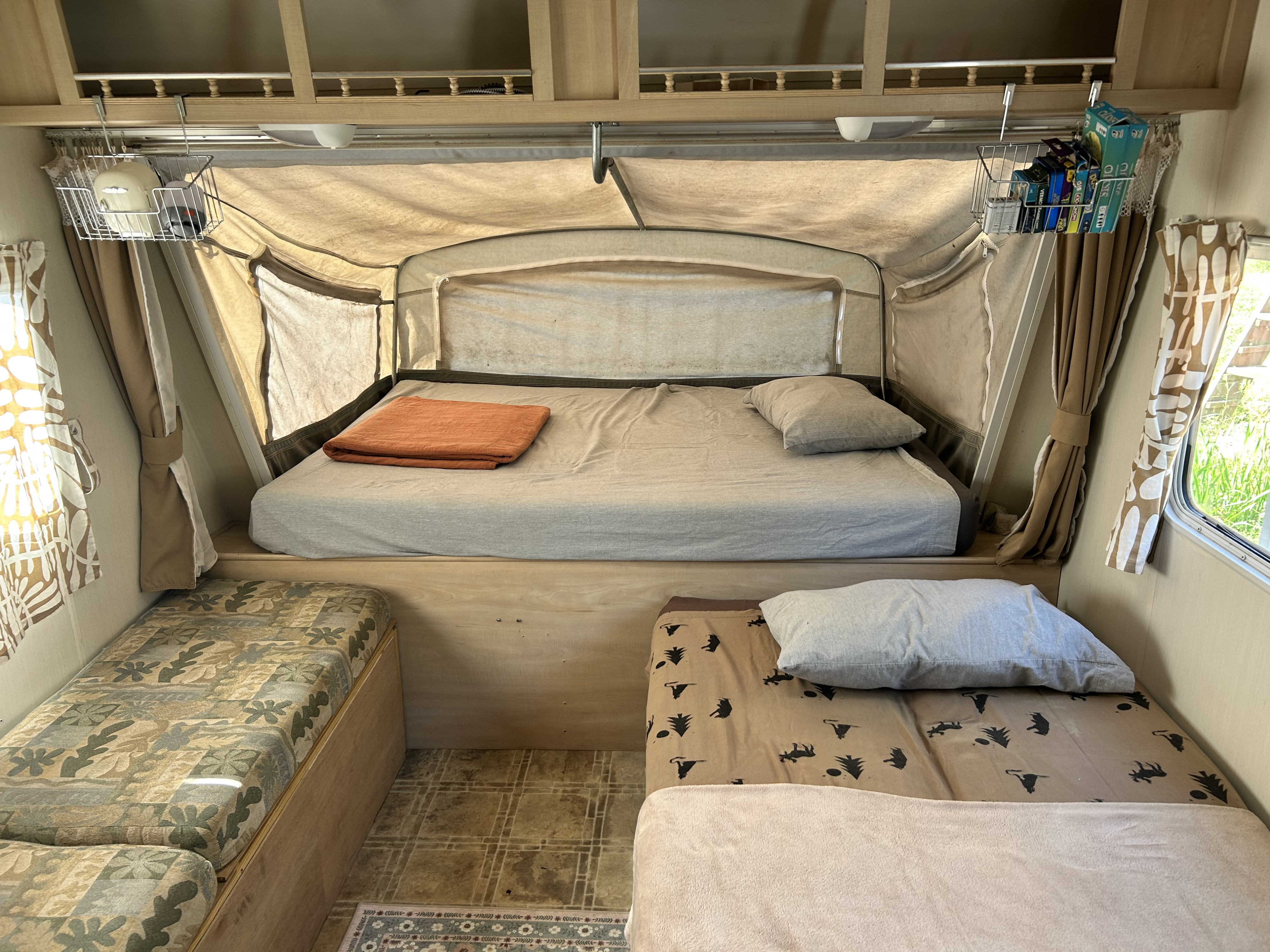 Cozy RV rental interior with main bed, side bed, and storage baskets, perfect for a relaxing camper adventure.. Forest River Surveyor 2003