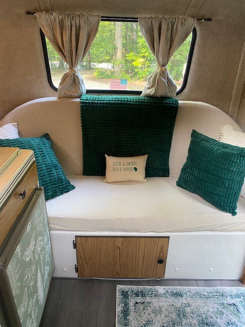 Cozy RV rental interior with comfy seating, green decor, Wisconsin-themed pillow, and scenic window view.. Scamp Scamp Trailer 1999