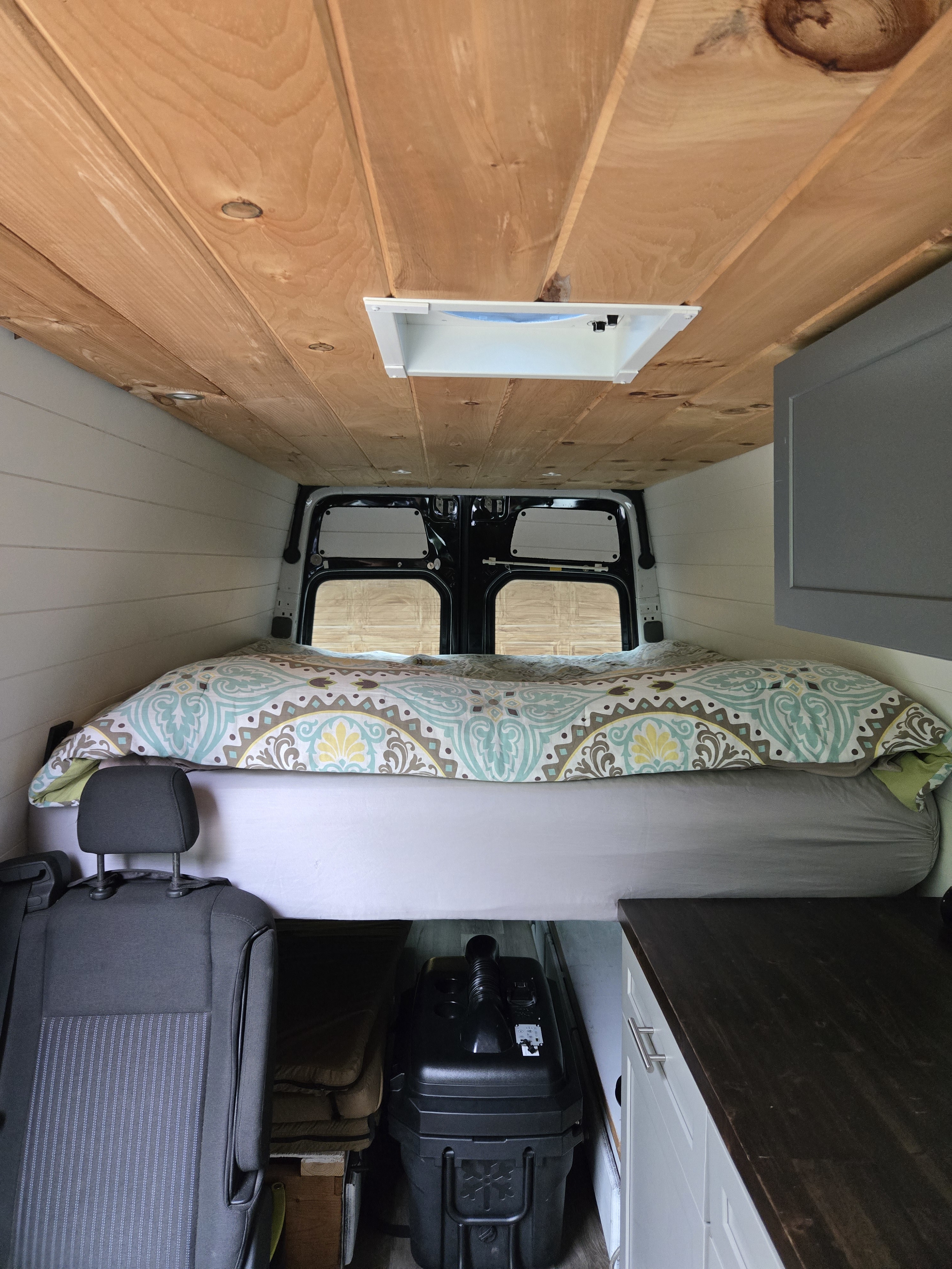 Inside an RV rental, featuring a raised bed, warm wood ceiling, rear windows, and kitchen cabinetry.. Freightliner Sprinter 2011