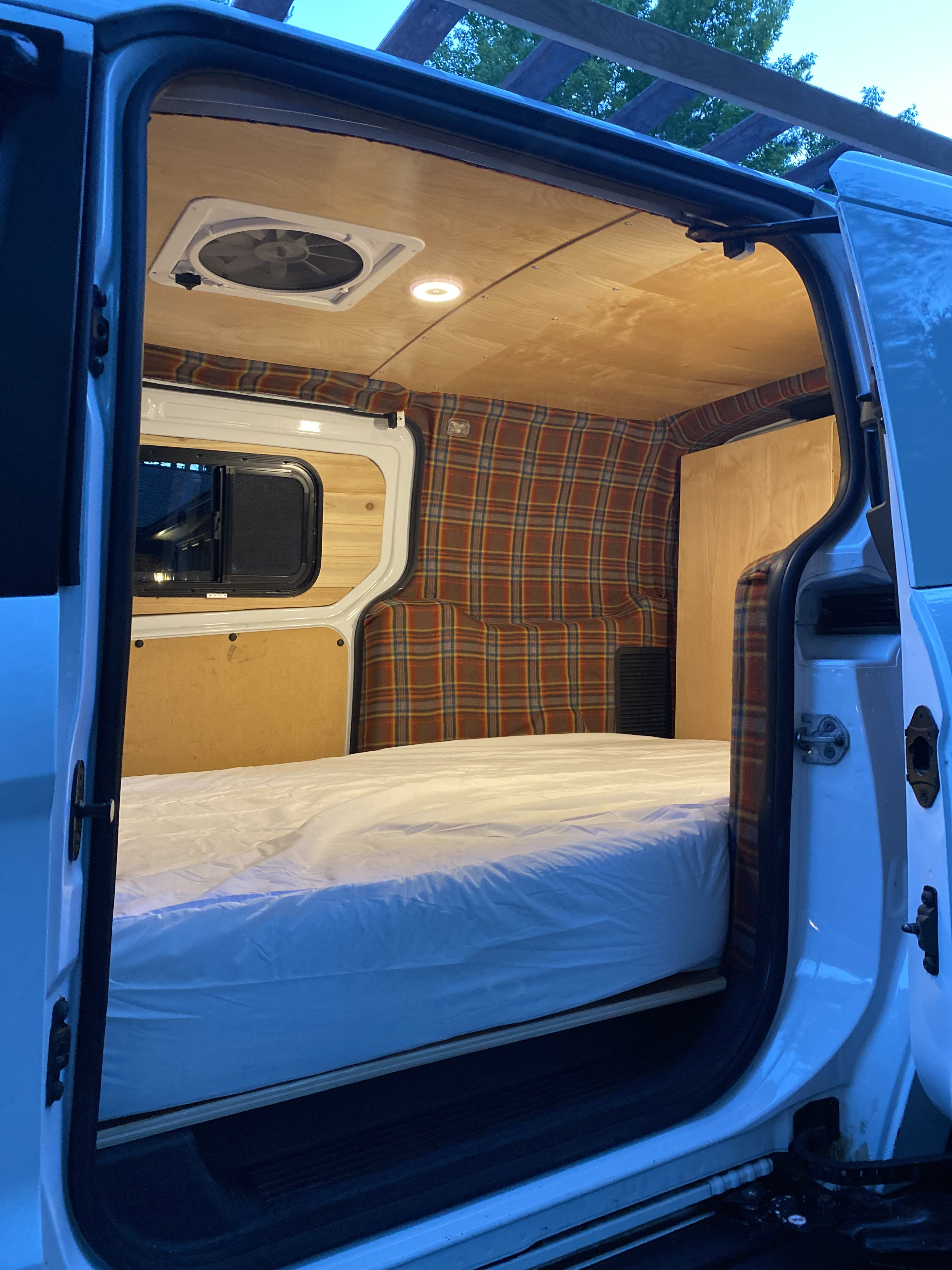 Cozy RV rental interior: bed, plaid walls, wood ceiling, fan, and window visible from the open door.. Ford Transit Custom 2015