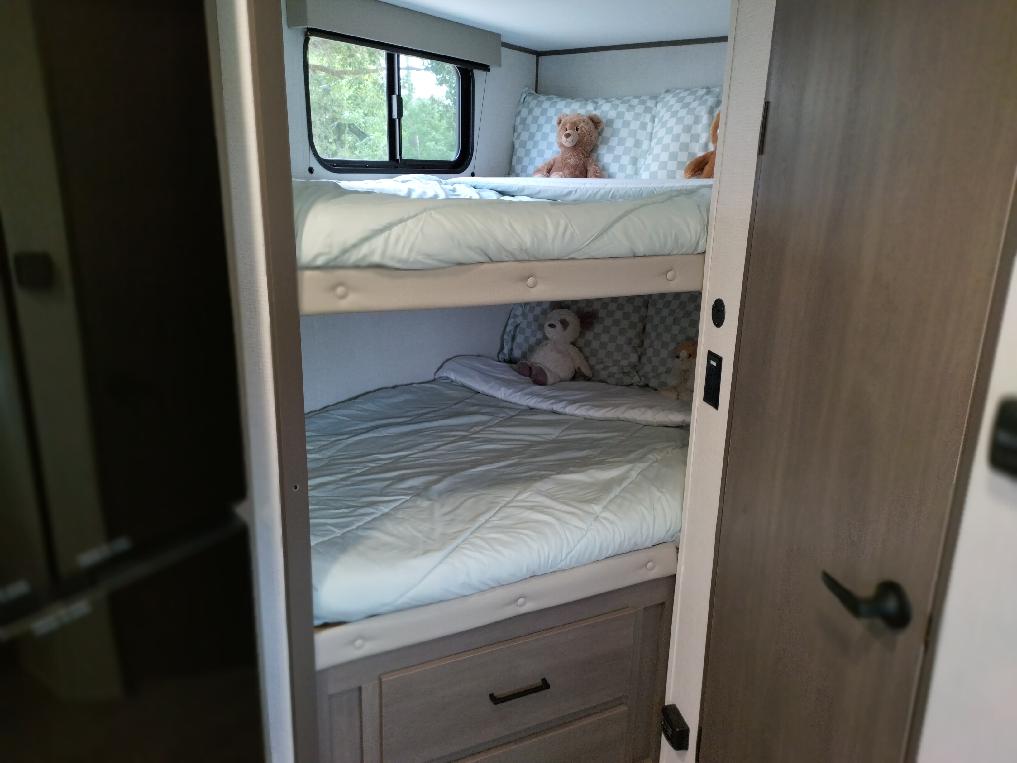 An RV rental's cozy interior featuring bunk beds, teddy bears, a scenic window, and practical storage drawers.. Grand Design Transcend One 161BH 2025