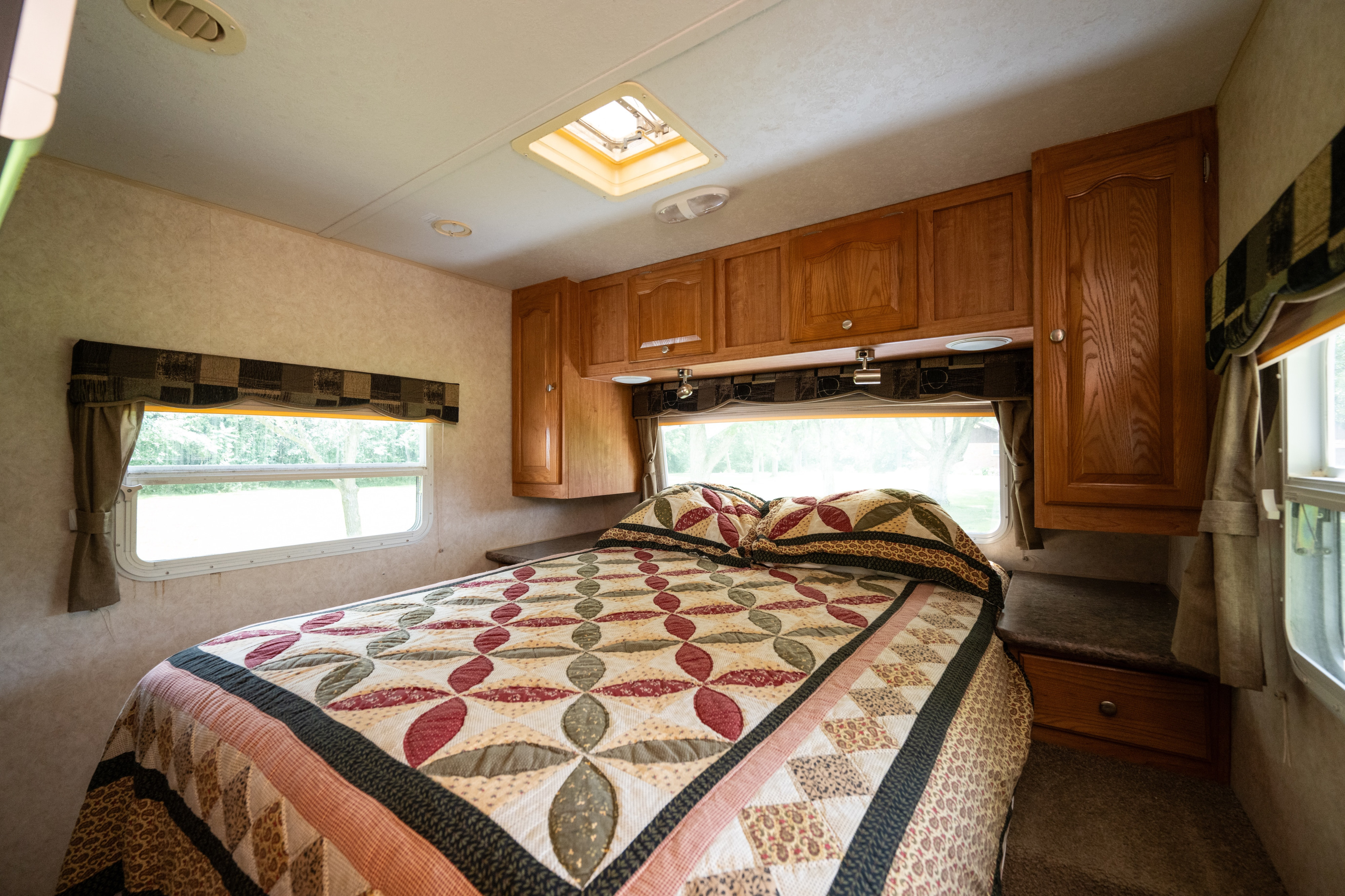 Bright RV rental bedroom: large bed with a colorful quilt, overhead wooden cabinets, and windows with scenic views.. Forest River Rockwood Signature Ultra Lite 2009