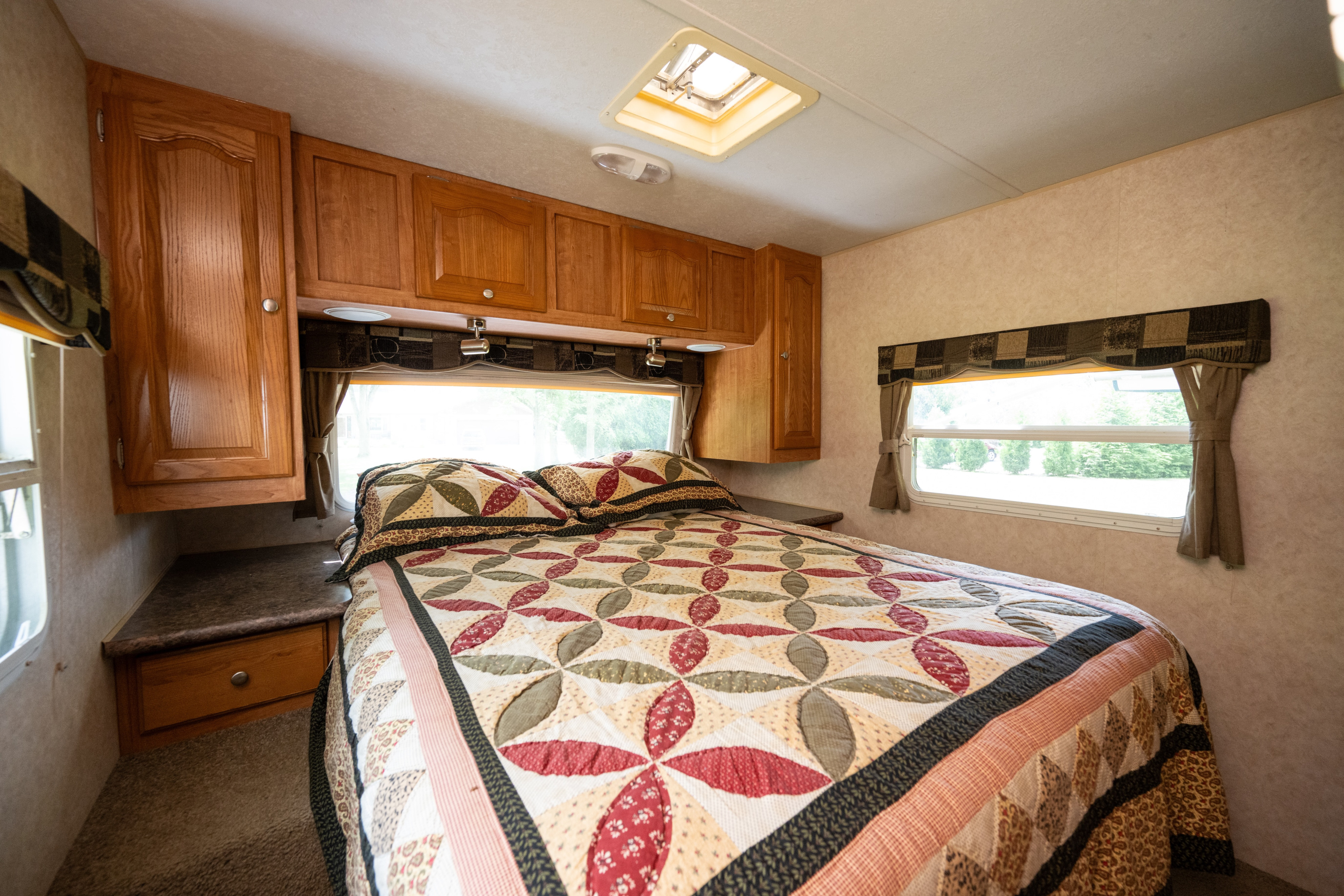 Inside a comfortable RV rental bedroom, featuring a large bed with a unique quilt, storage cabinets, and natural light.. Forest River Rockwood Signature Ultra Lite 2009