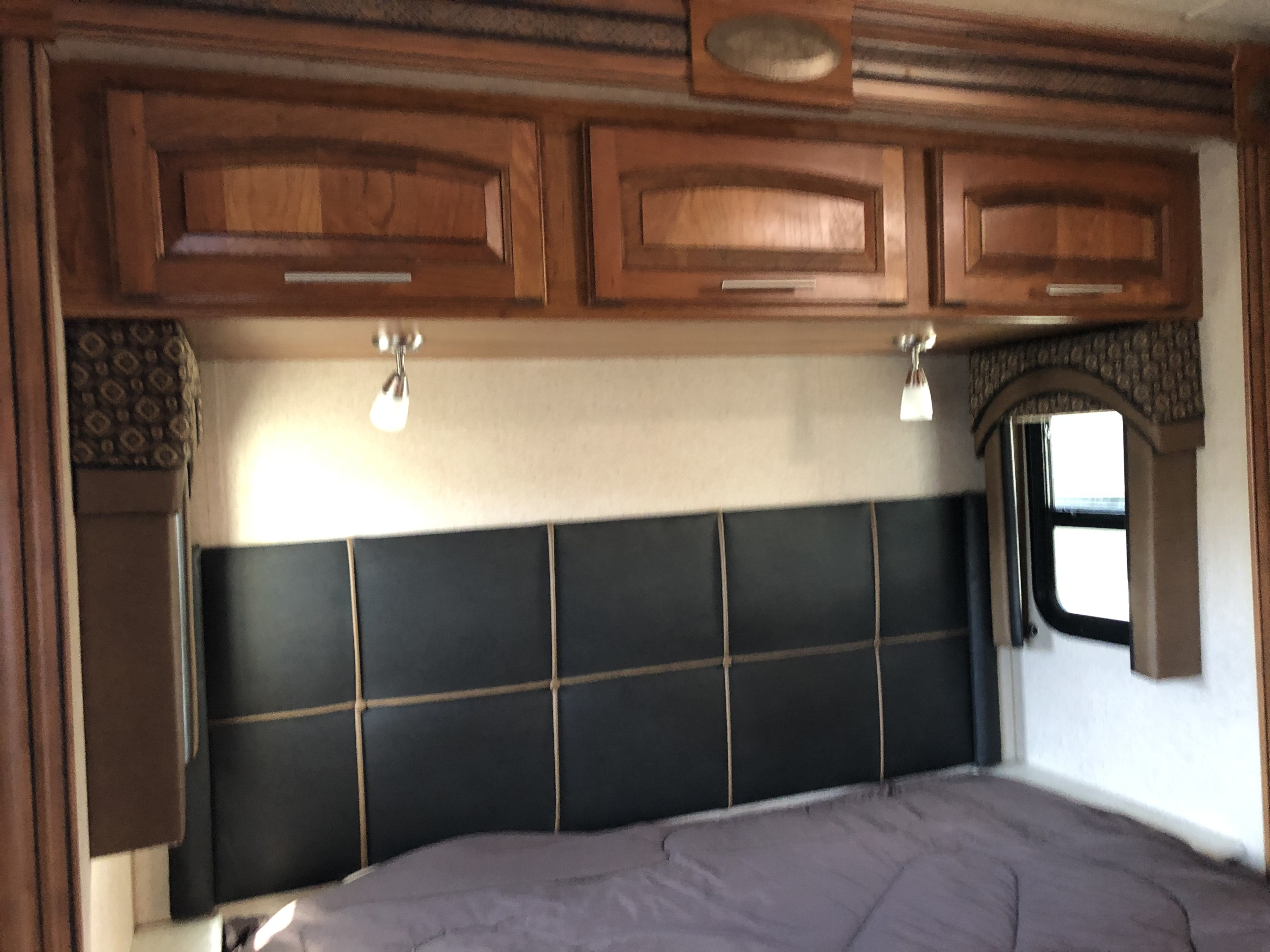 Comfortable RV rental bedroom with overhead cabinets, a padded headboard, and reading lights.. Jayco Precept 2018