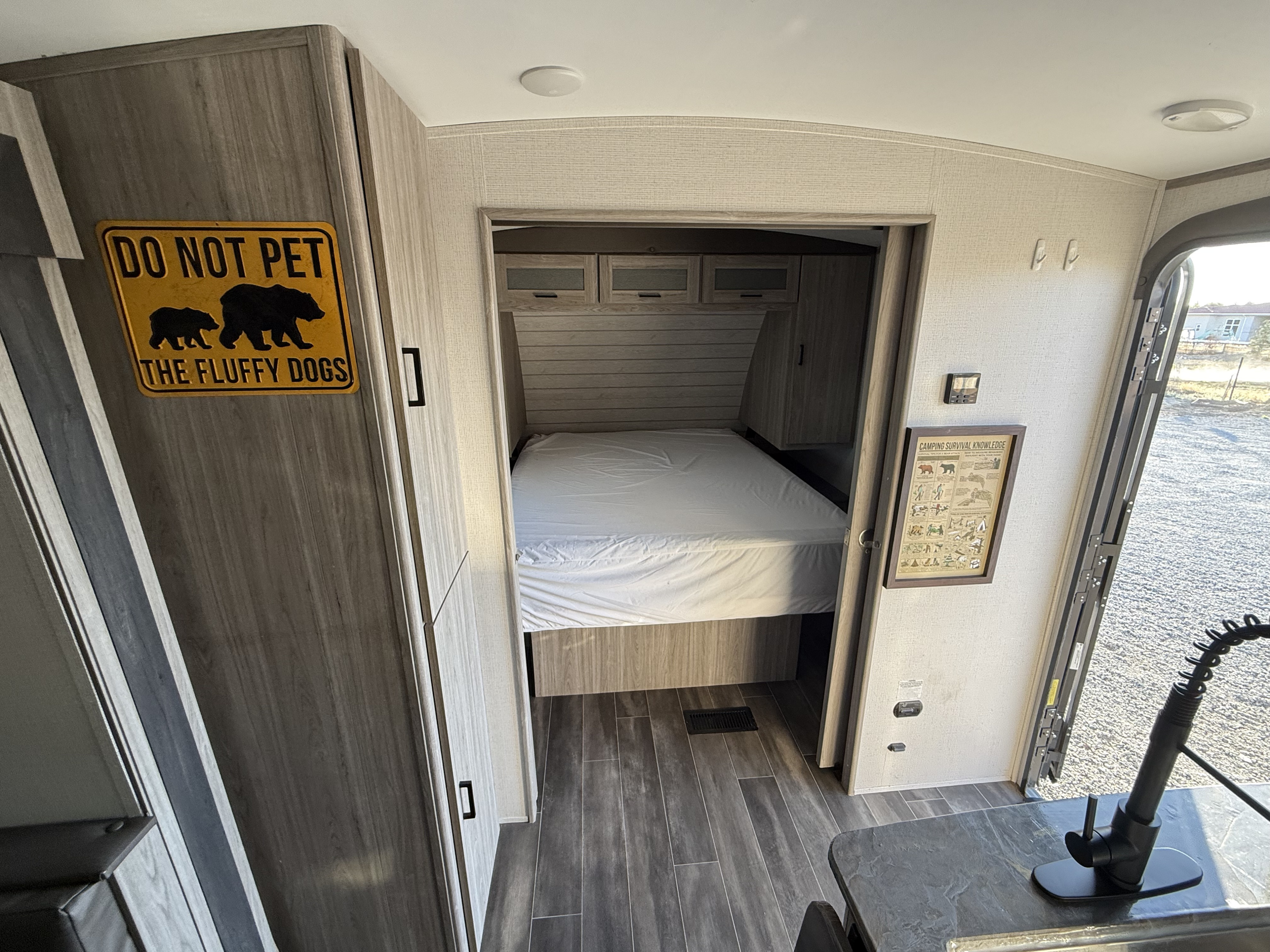 RV rental interior features a sleeping nook, wood flooring, a kitchen counter, and a fun "fluffy dogs" bear sign.. Keystone RV Passport GT 2022