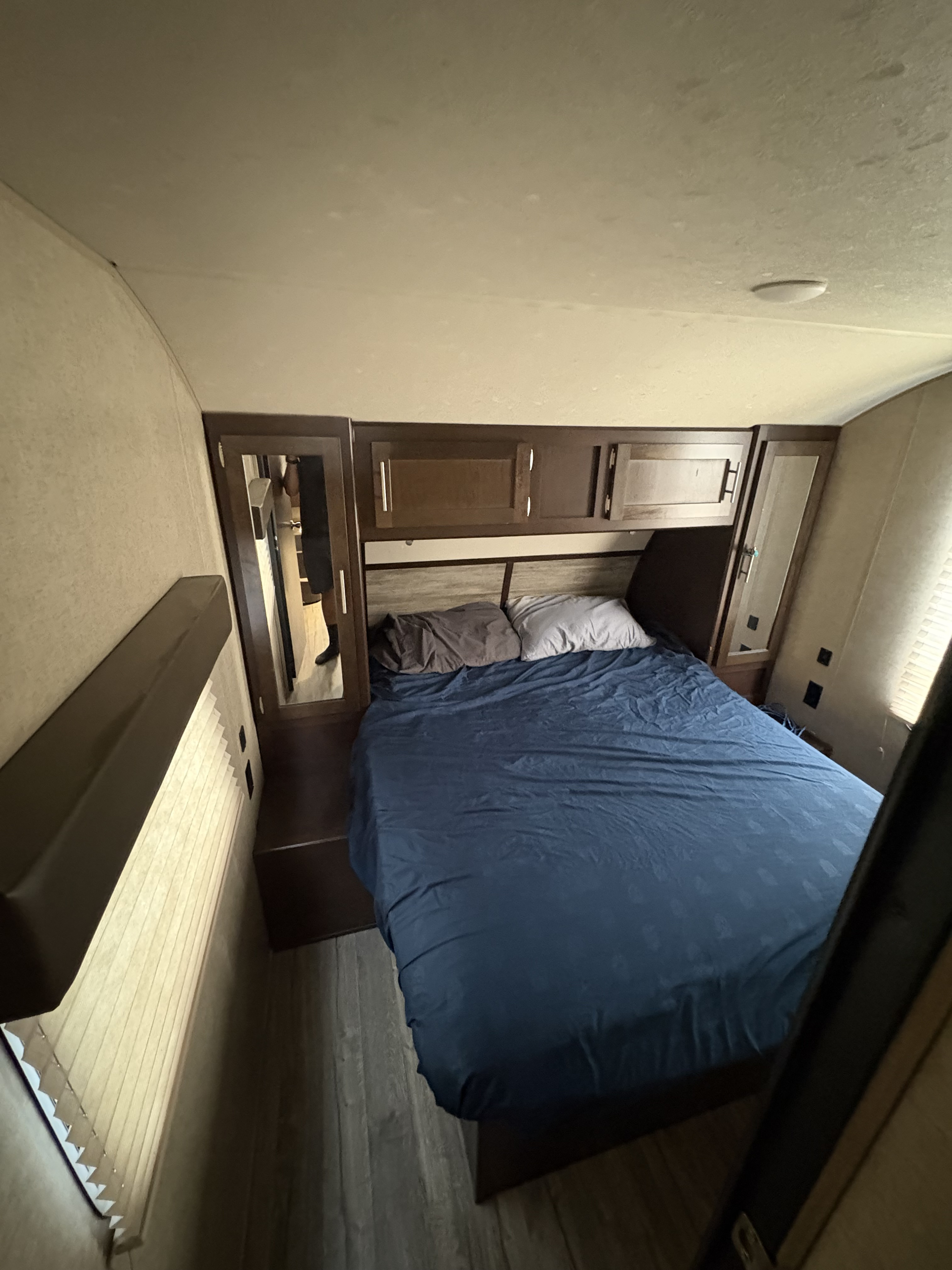 An RV rental's compact bedroom features a bed with blue bedding, built-in cabinets, and a mirrored closet.. Forest River Cherokee Grey Wolf 2018