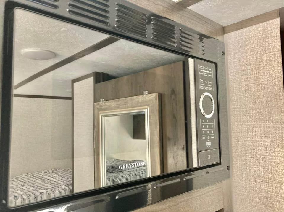 RV rental: Close-up of microwave reflecting a modern bunk bed, cozy sleeping area, and framed mirror.. Dutchmen Coleman Lantern LT 2021