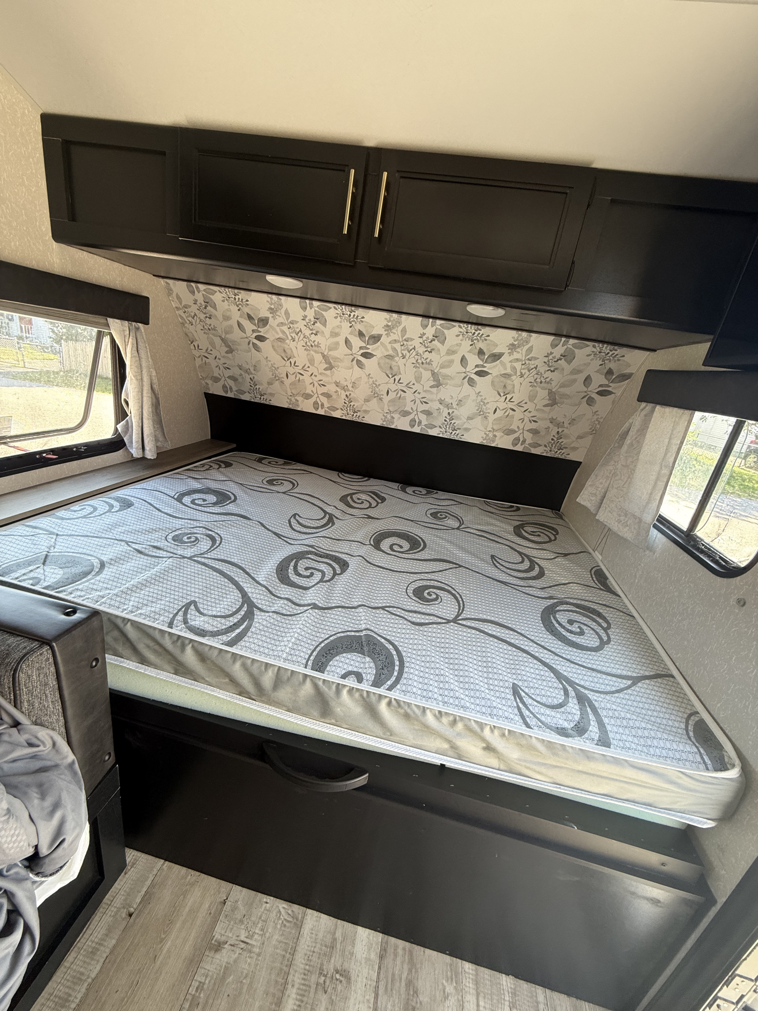 Inside an RV rental: a cozy bedroom with a patterned mattress, dark overhead cabinets, wall decor, and side windows.. Forest River Cherokee Wolf Pup 2022