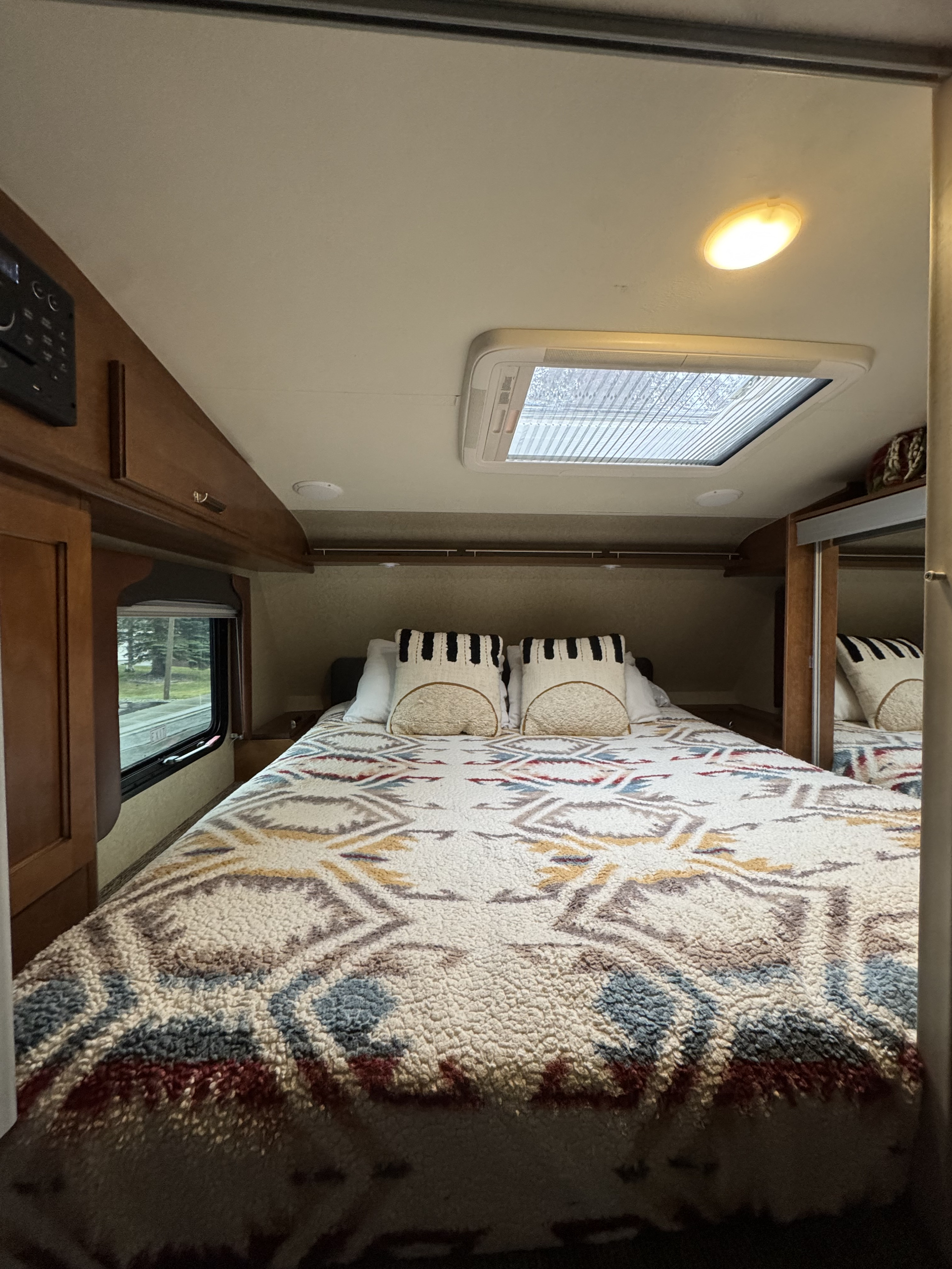 Cozy RV rental bedroom interior with patterned blanket, skylight, and window view.. Lance 1172 2017