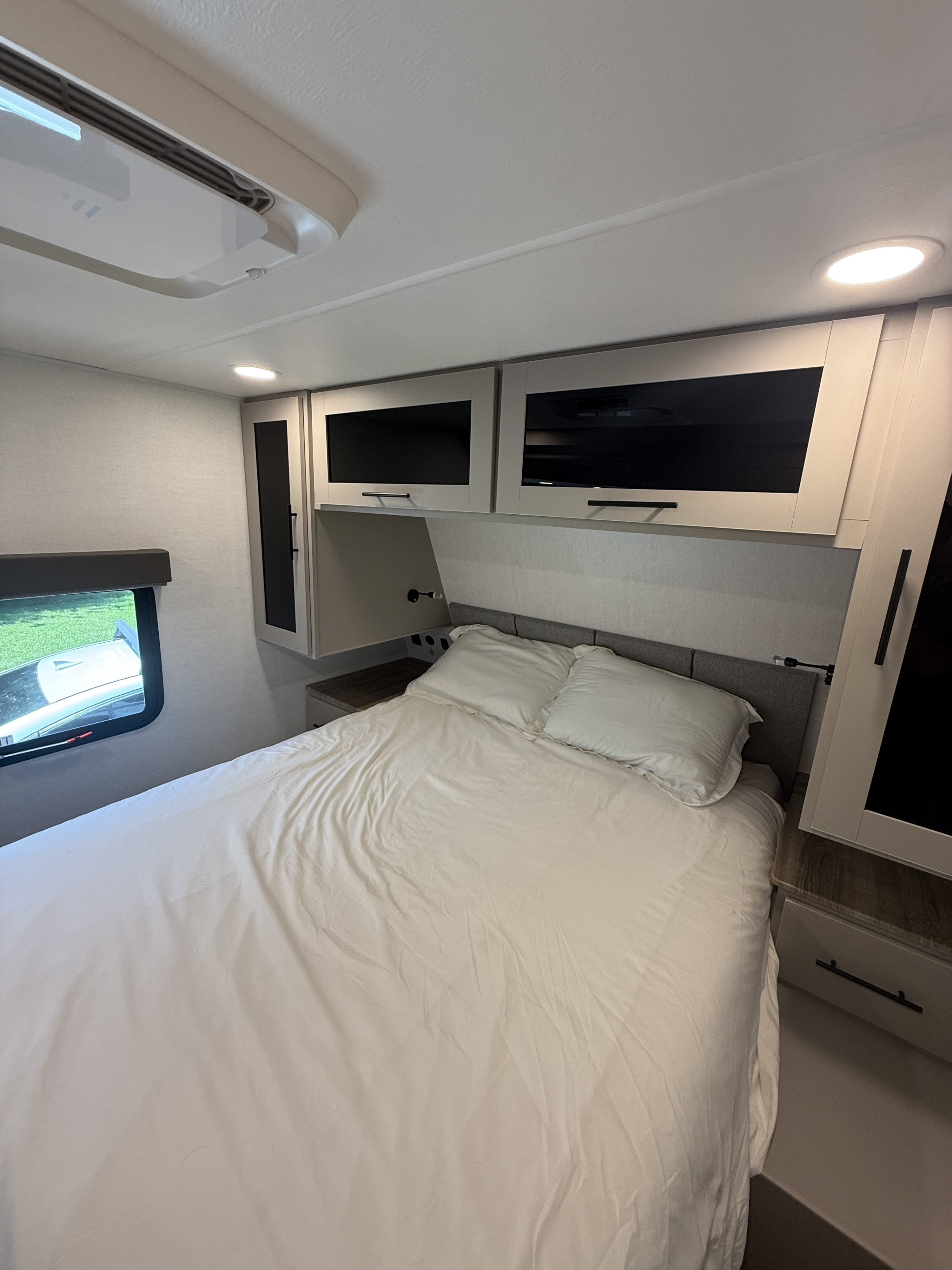 Relaxing RV rental bedroom with white bedding, sleek overhead cabinets, AC, and a scenic window view.. Alliance Delta 2026