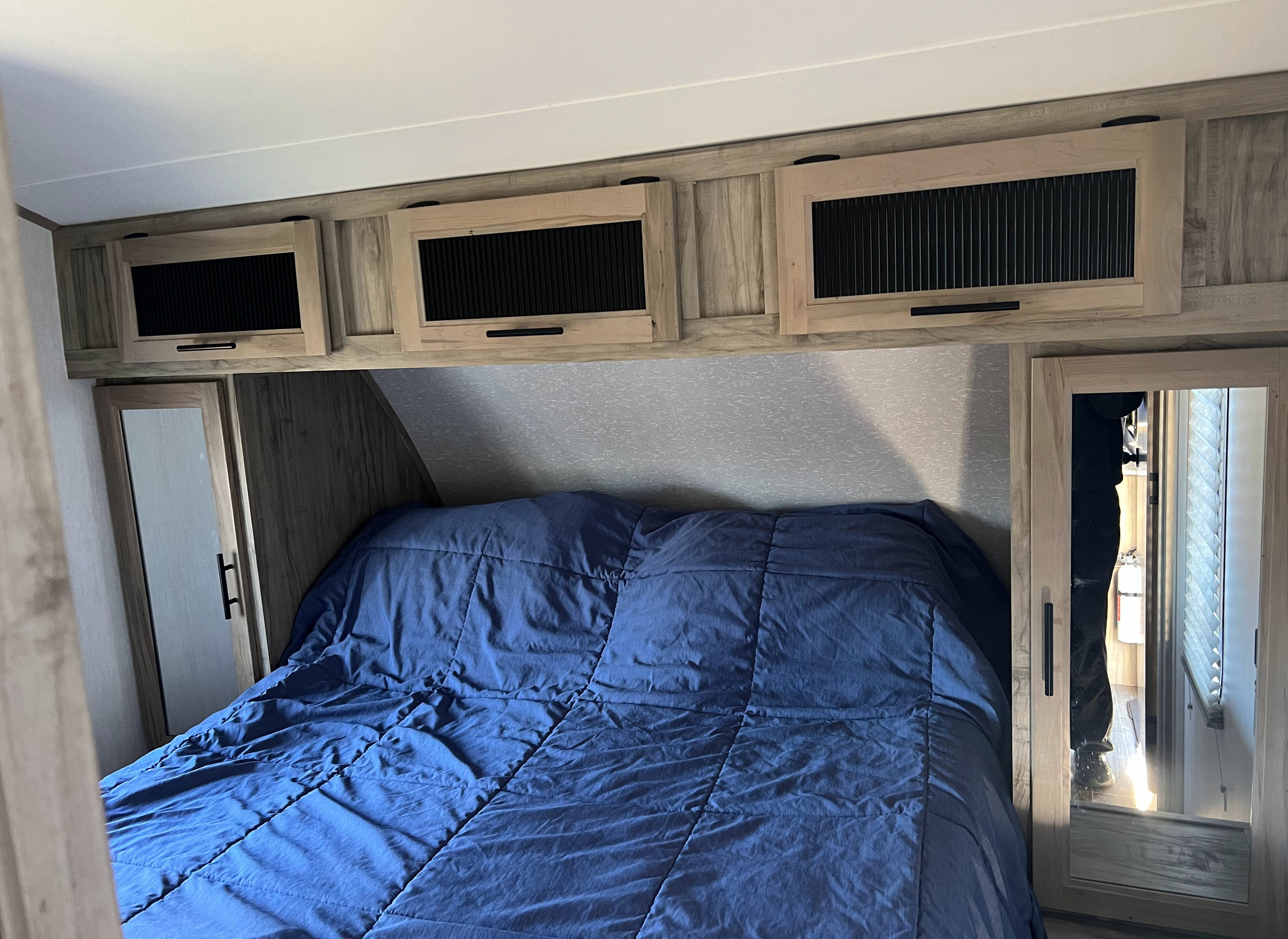 This RV rental bedroom features a comfy blue bed, practical overhead cabinets, and a mirrored closet for essential storage.. Forest River Cherokee Alpha Wolf 2022