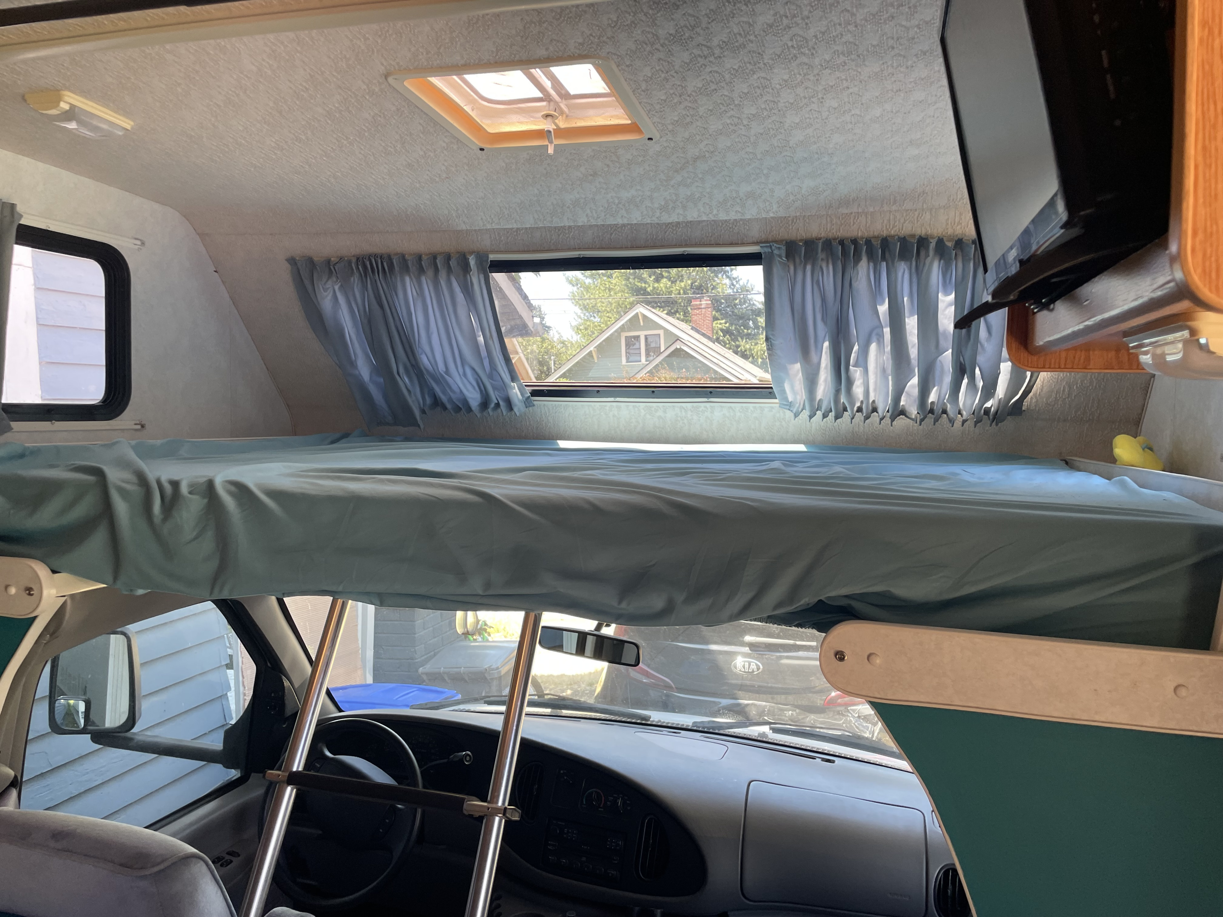 RV rental interior featuring a cozy overhead bunk bed, skylight, and dashboard view from a parked motorhome.. Winnebago Minnie Winnie 2001