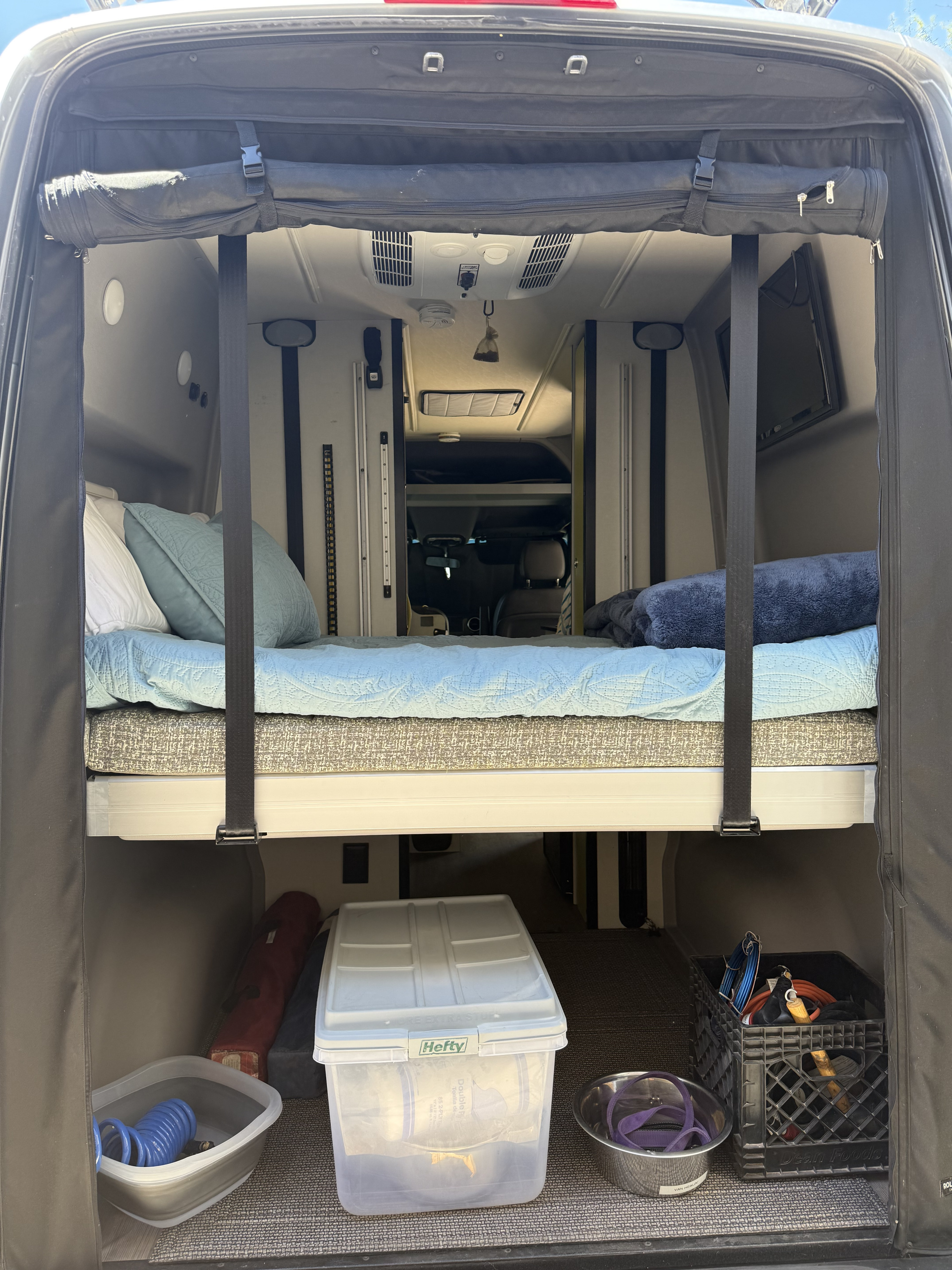 RV rental: Camper van's rear showing a bed, overhead AC, and under-bed storage with supplies.. Winnebago Revel 2020