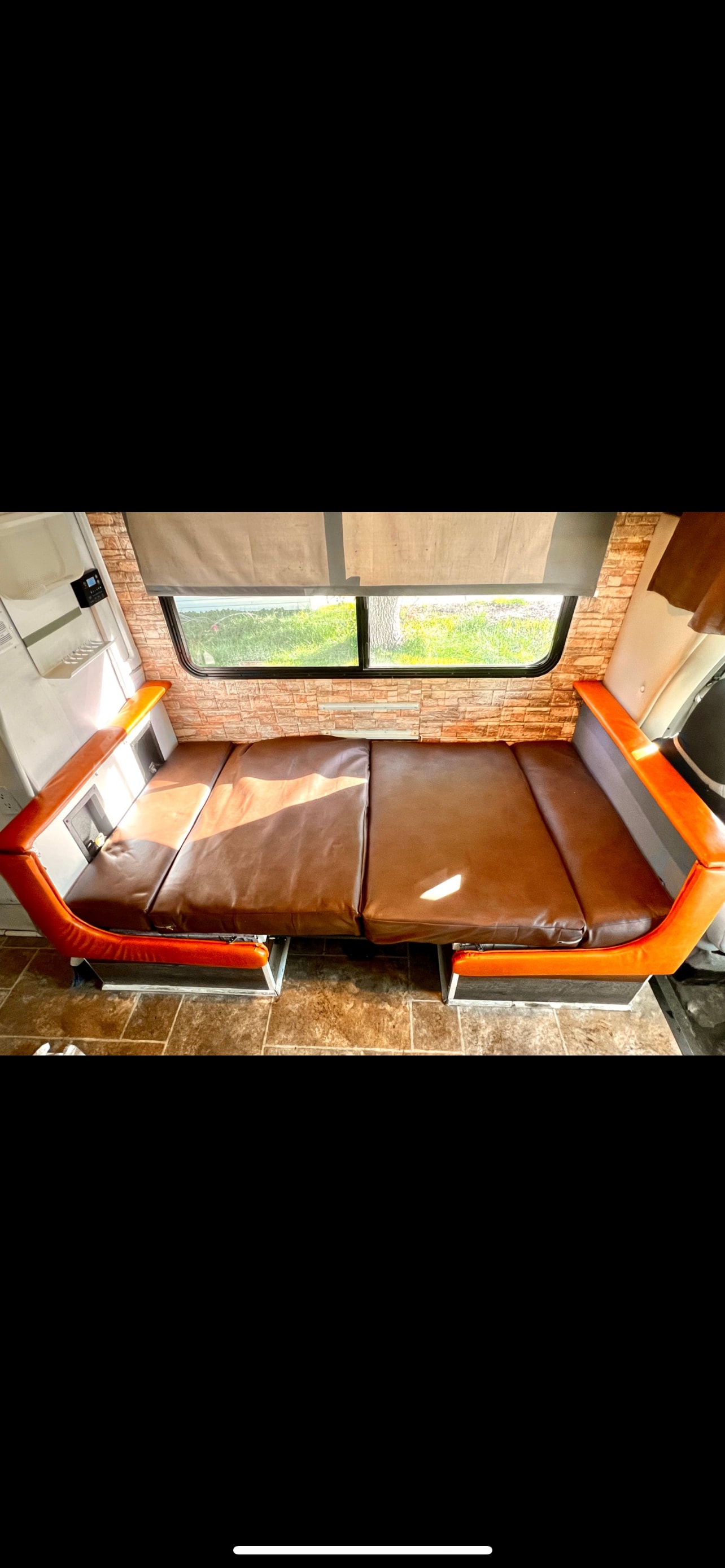 Bright RV rental interior showing brown cushioned seating/bed, a window with outdoor view, and brick-patterned wall.. Four Winds Majestic 2009