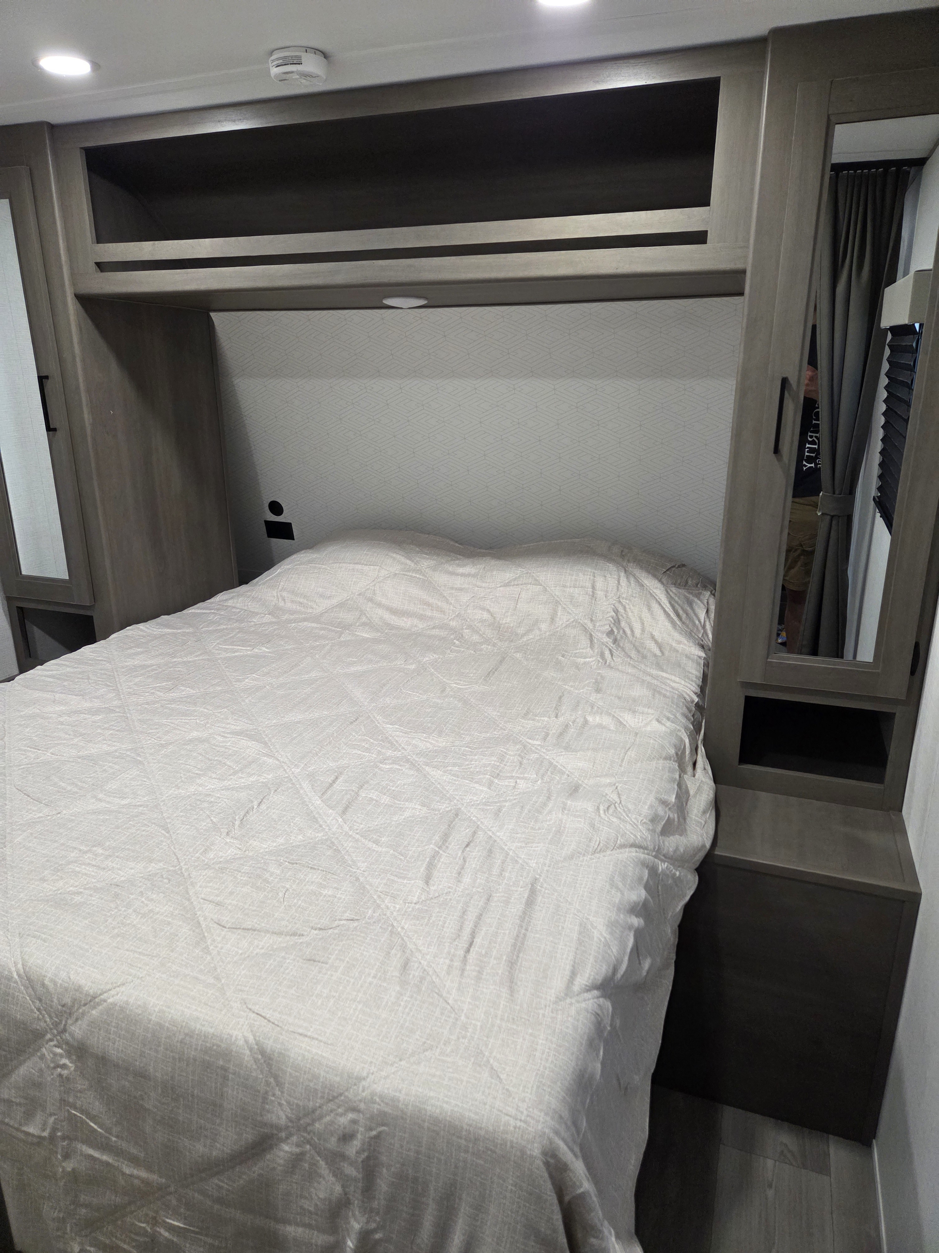 Inside an RV rental, this cozy bedroom features a comfortable bed, practical overhead storage, and built-in side cabinets.. Grand Design Transcend Xplor 2025