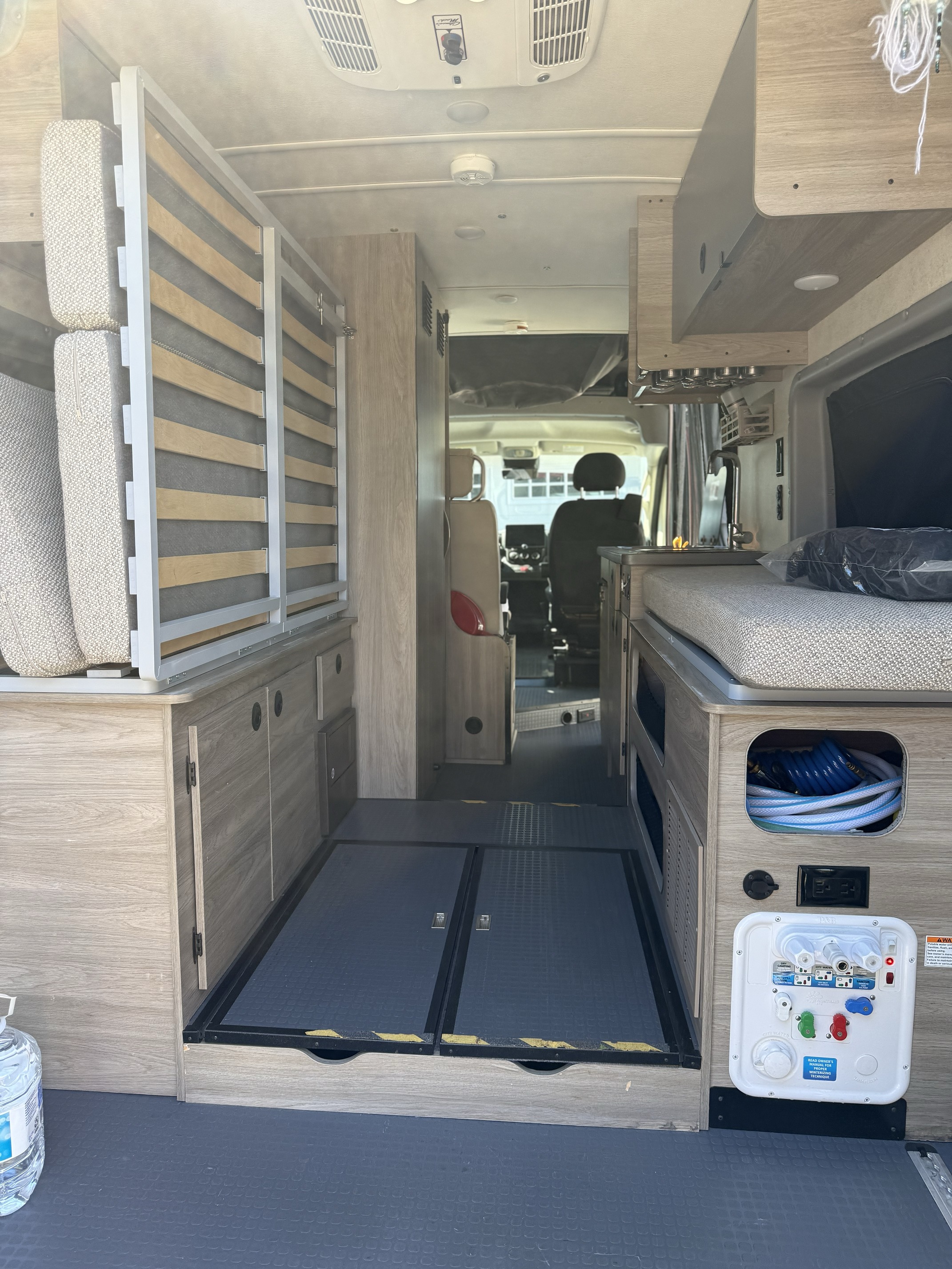 Inside an RV rental: a modern interior with convertible bed/storage, compact kitchen, and flooring hatches, facing the cockpit.. Winnebago Solis 2021