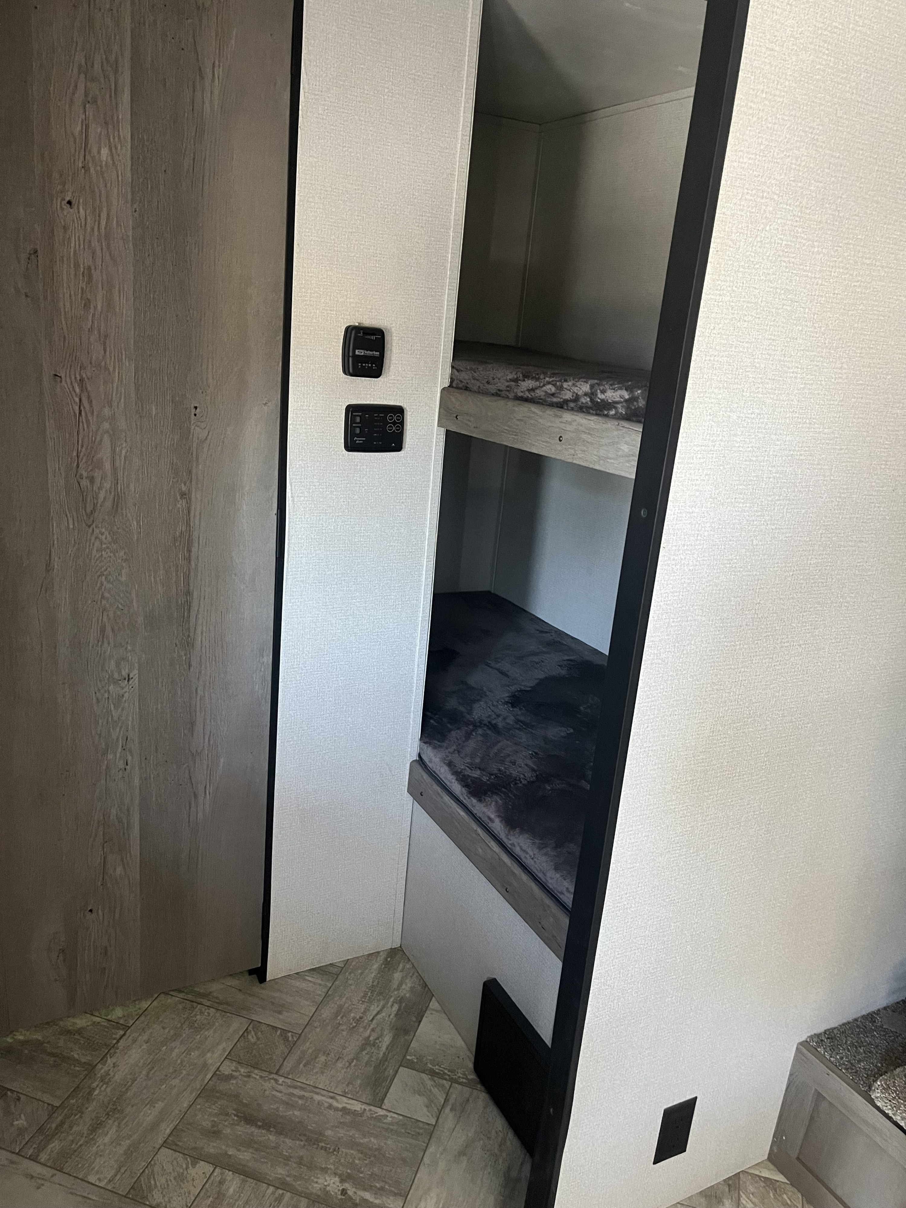 Inside an RV rental, featuring bunk beds, wood-look walls, and climate controls for comfortable travel.. Keystone RV Springdale 2021