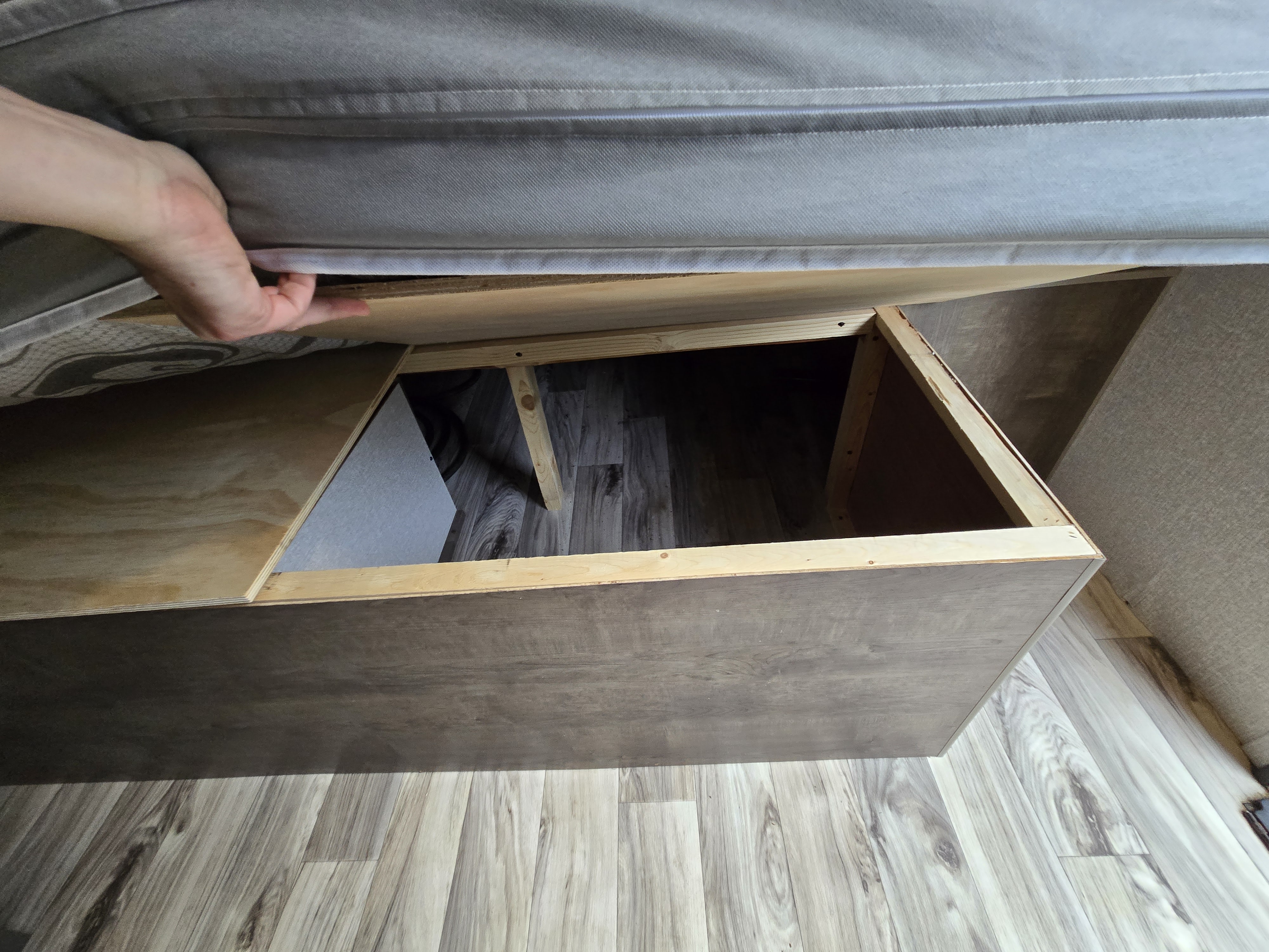 RV rental under-bed storage: A hand lifts the mattress to show a wooden compartment above laminate flooring.. Sonic Lite 2022