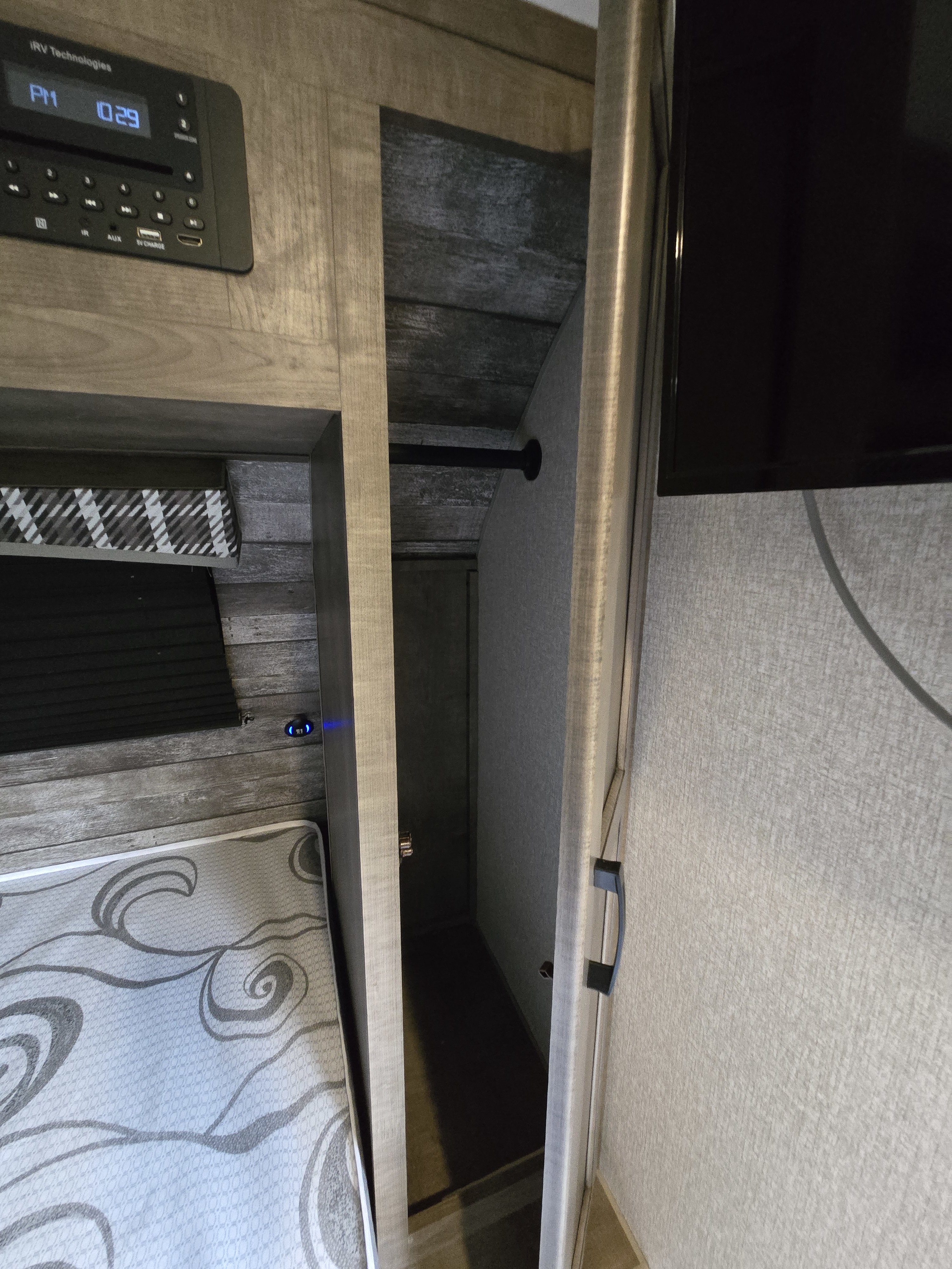 An RV rental bedroom showcasing a media unit (10:29 PM), patterned bed, open closet with hanging bar, and wall-mounted TV.. Sonic Lite 2022