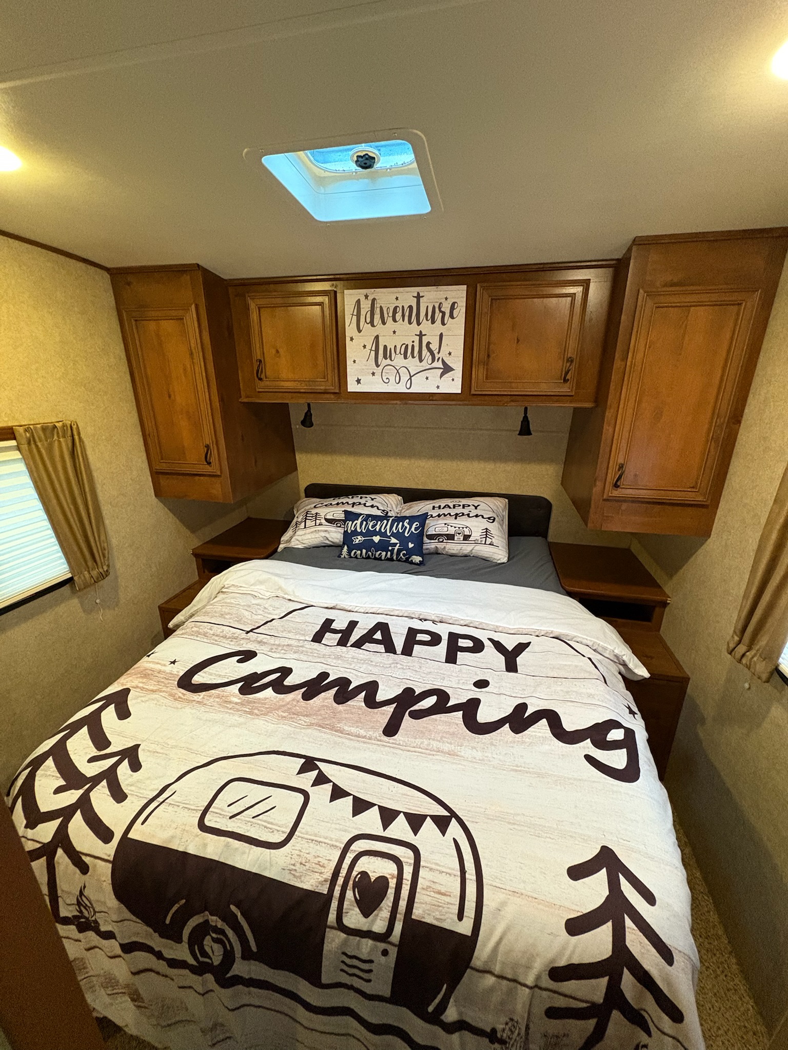 An inviting RV rental bedroom with "Happy Camping" bedding and "Adventure Awaits" decor, perfect for your next camping adventure.. Open Range RV Light 2014