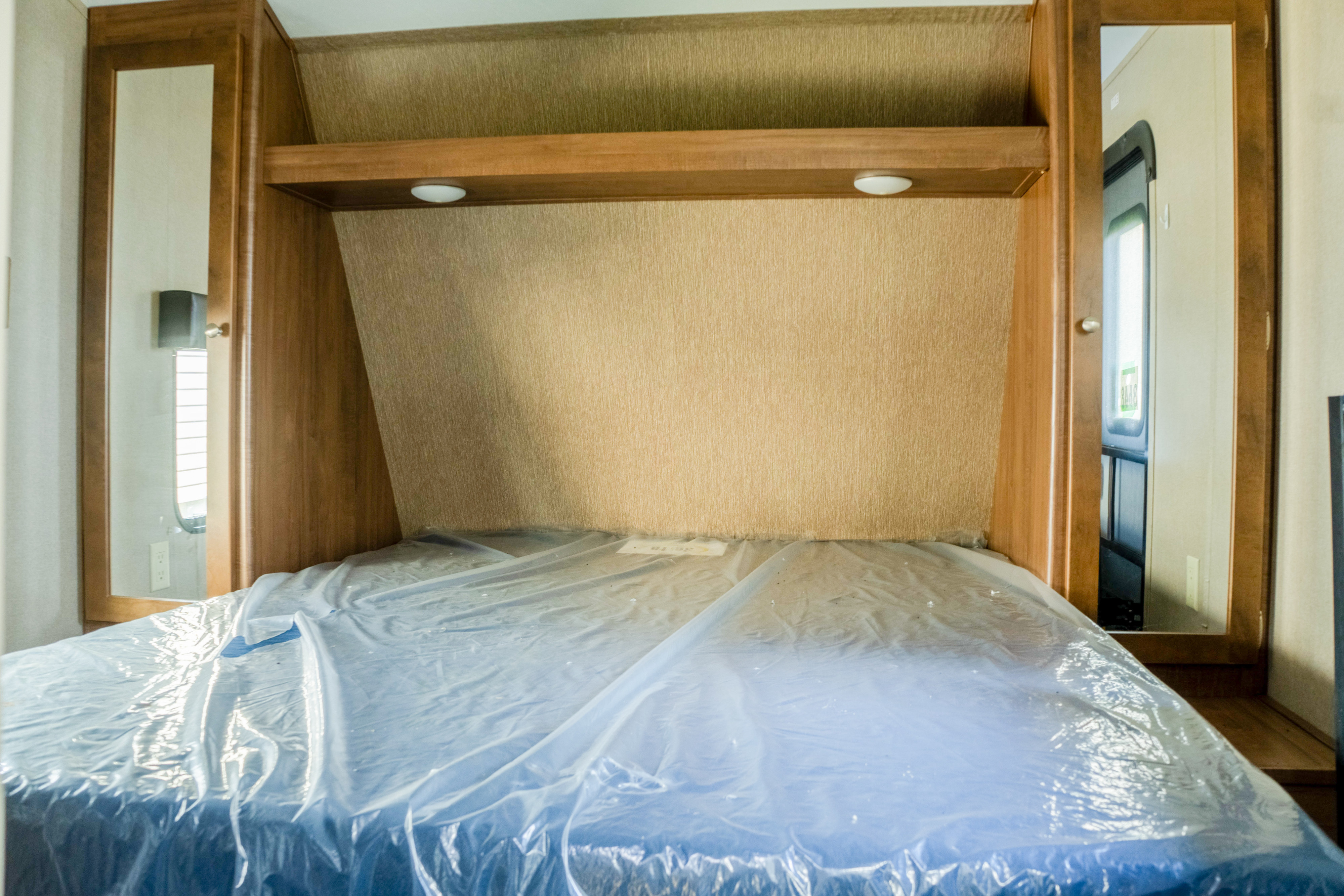 RV rental bedroom features a new, plastic-covered bed, overhead shelf with lights, and mirrored wardrobes on each side.. Aspen Trail Aspen Trail Trailer 2017