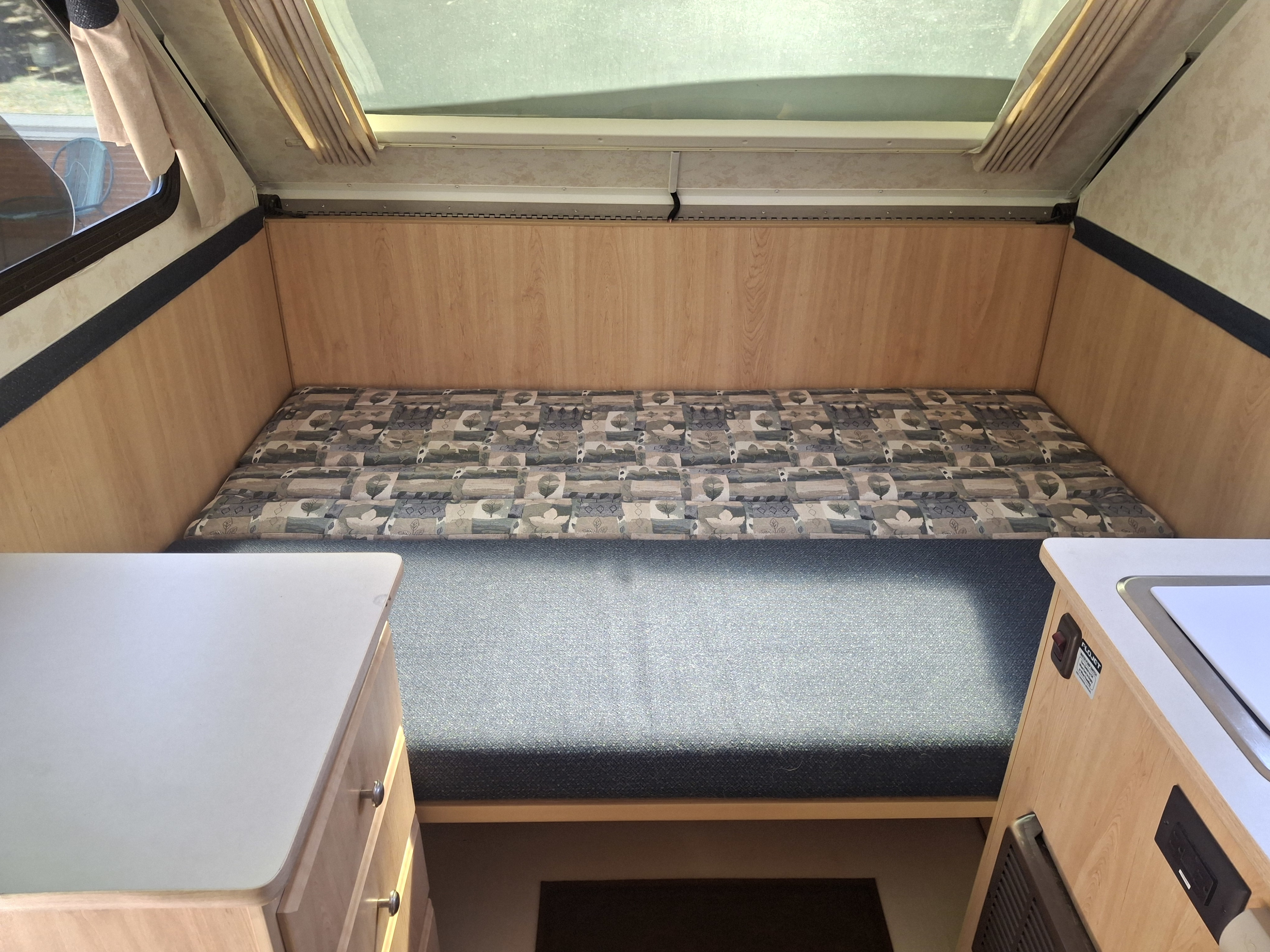 RV rental interior features a cozy bed/dinette, light wood counters, and a pop-up roof with ample natural light.. Chalet Chalet Popup Trailer 2006